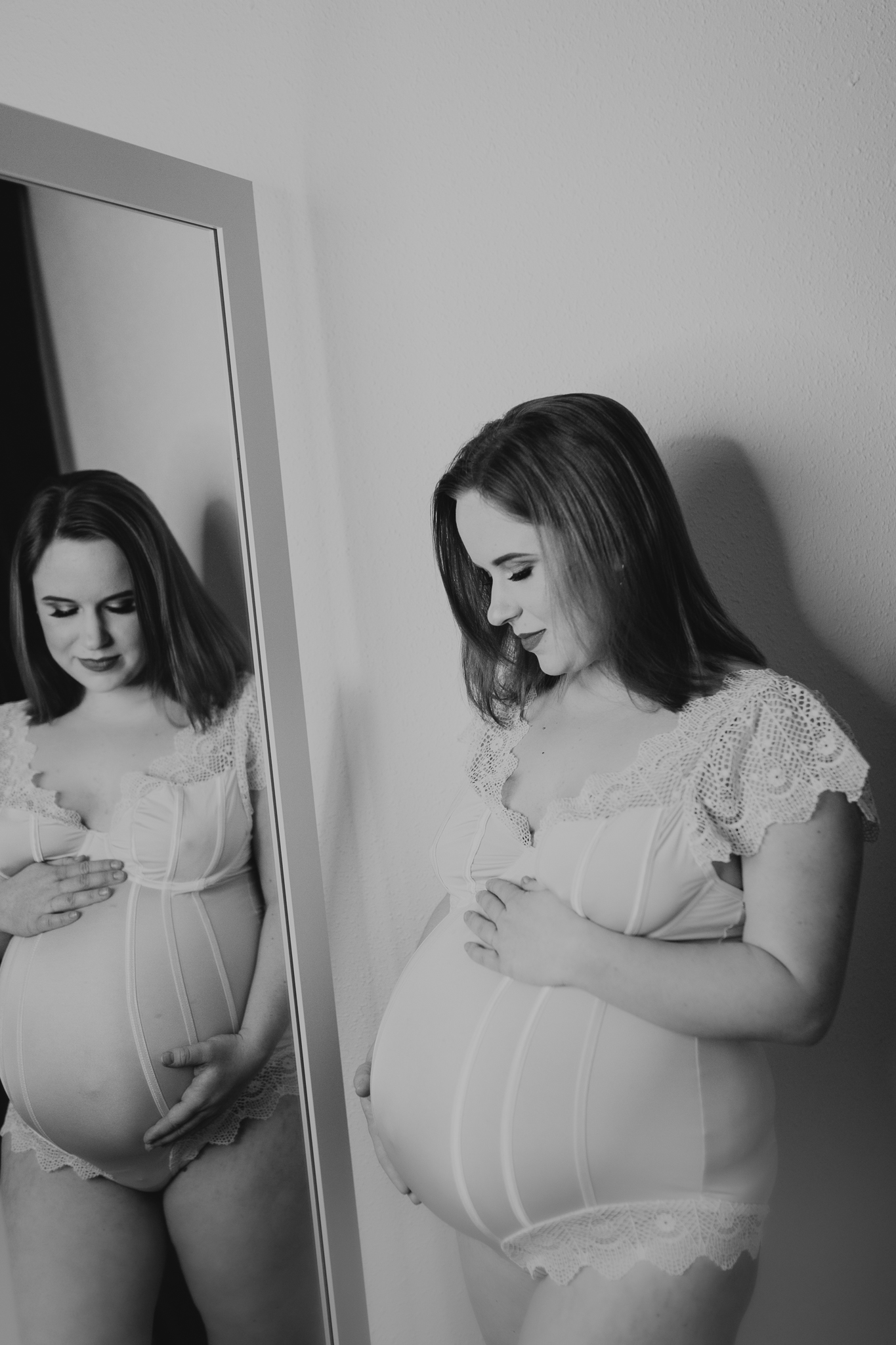 Kobieta w ciąży oparta o ścianę spogląda w swoje odbicie lustrzane