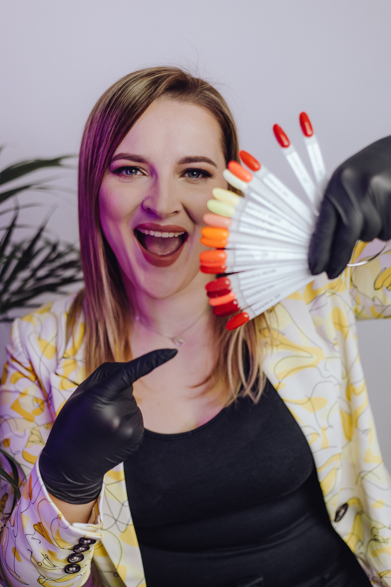 Uśmiechnięta kobieta trzyma w ręce paletę barw lakierów do paznokci