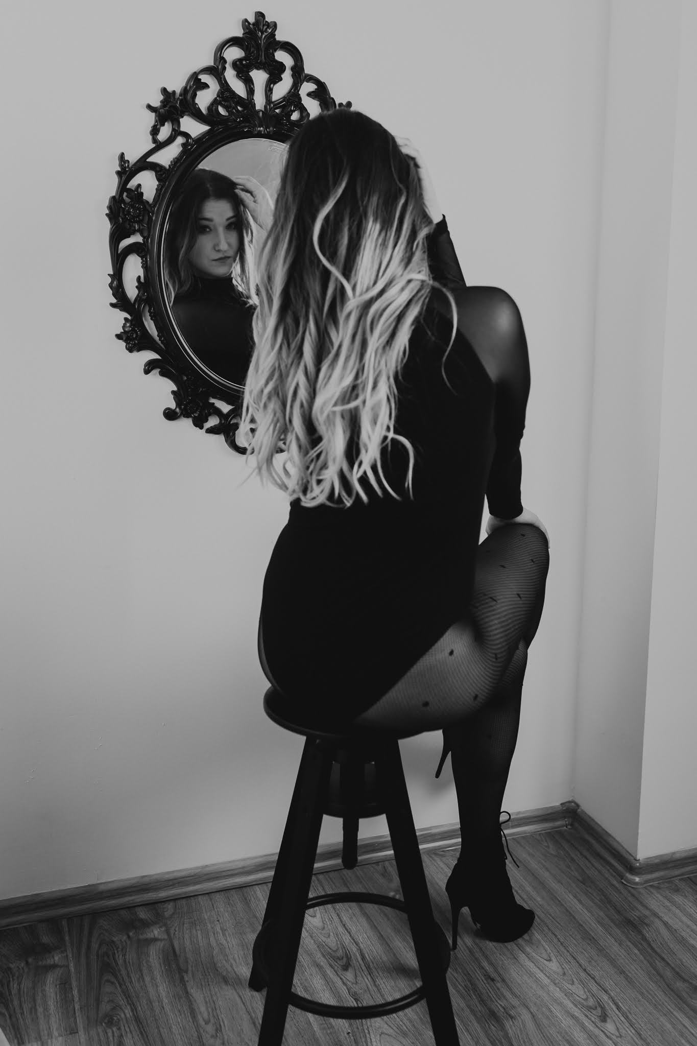 Kobieta siedzi na krześle i spogląda się w lustro na ścianie. Widzi swoje odbicie. Fotografia ekspresyjna