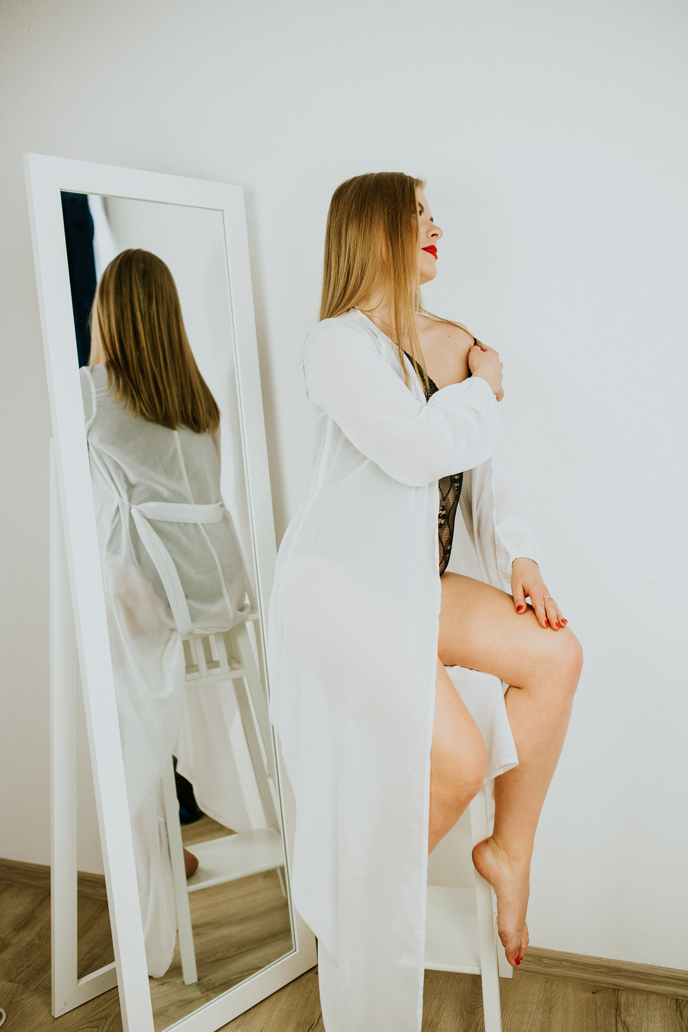 Kobieta w białym szlafroku, która odbija się tyłem w lustrze.