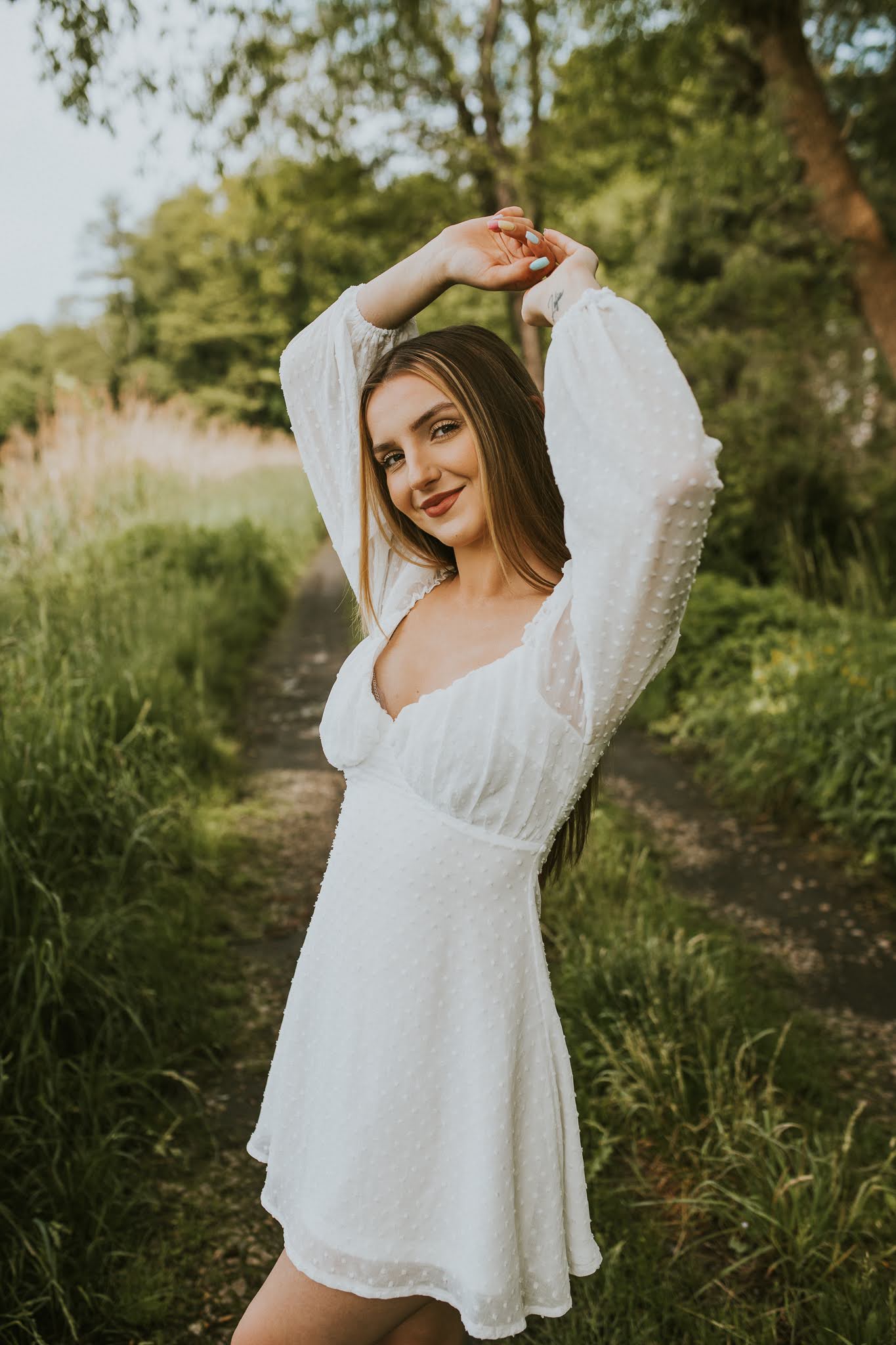 Uśmiechnięta dziewczyna z rękoma w górze w białej sukience