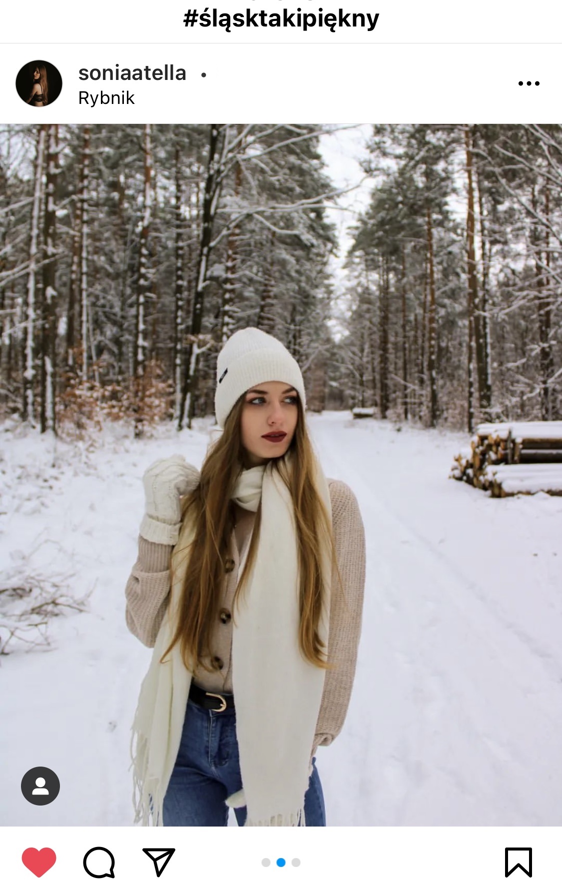 Dziewczyna w białym szaliku i białej czapce stoi na alei leśnej.