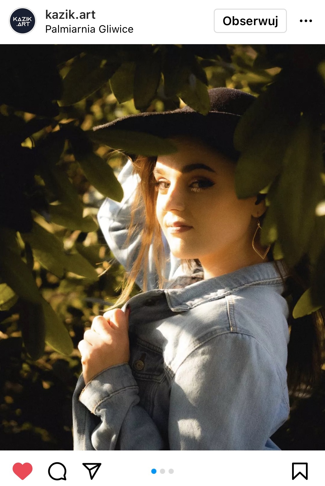 Dziewczyna stojąca w kapeluszu pośród drzewa. W twarz świeci jej słońce.