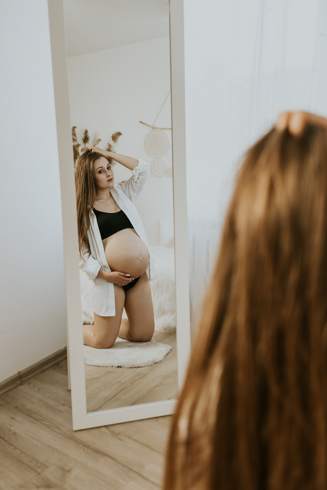 Kobieta klęcząca przed lustrem w odbiciu ciążowy brzuch