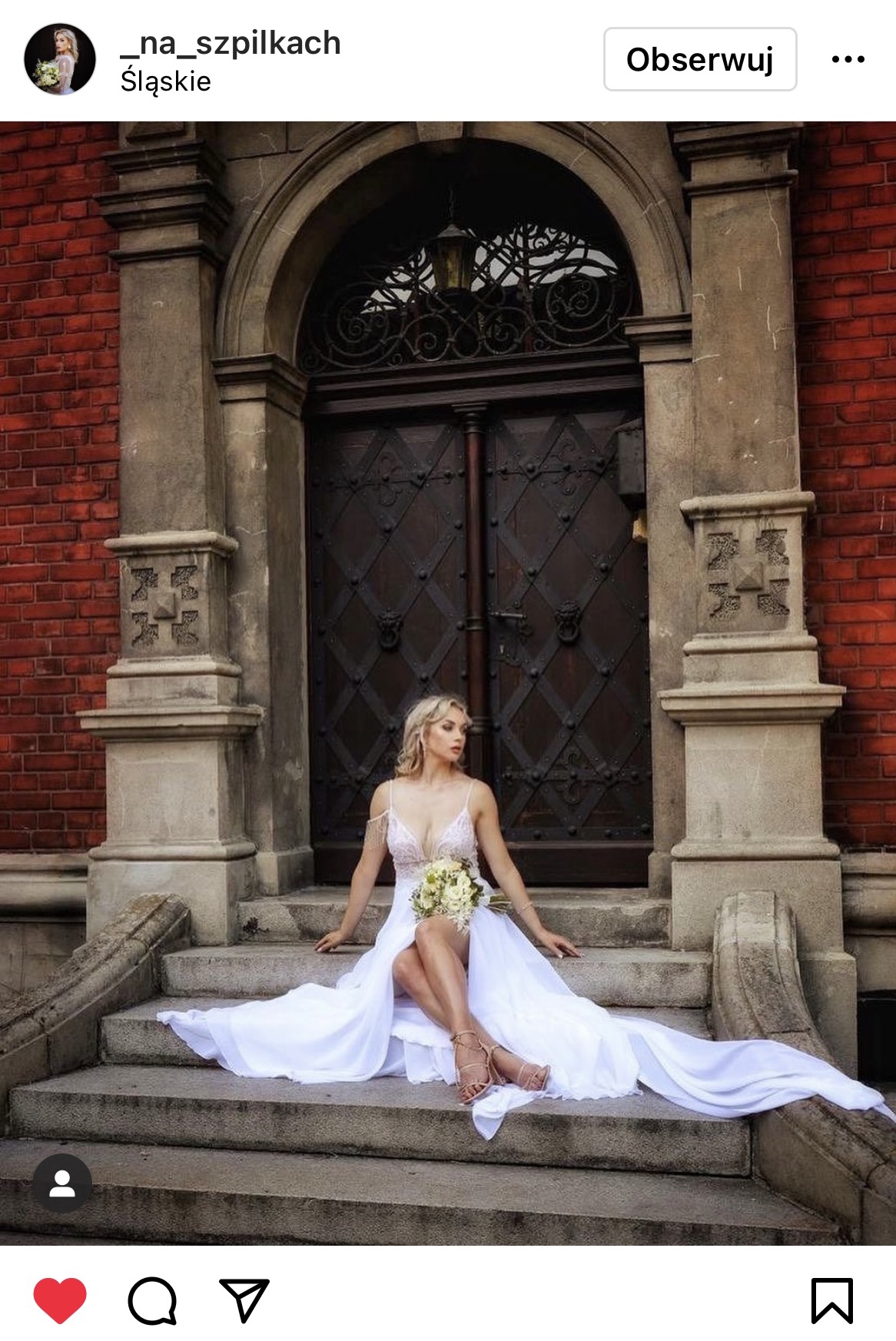 Kobieta w białej sukni siedzi na schodach przed dużymi metalowymi drzwiami. #śląsktakipiękny