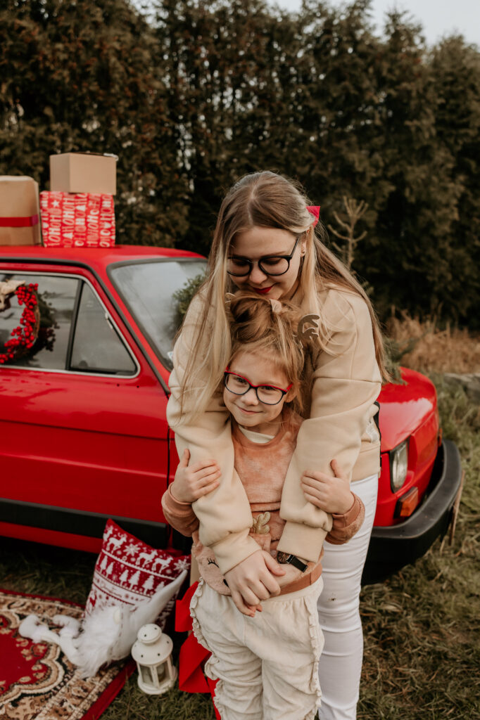 kobieta obejmuje małą dziewczynkę w tle czerwony samochód