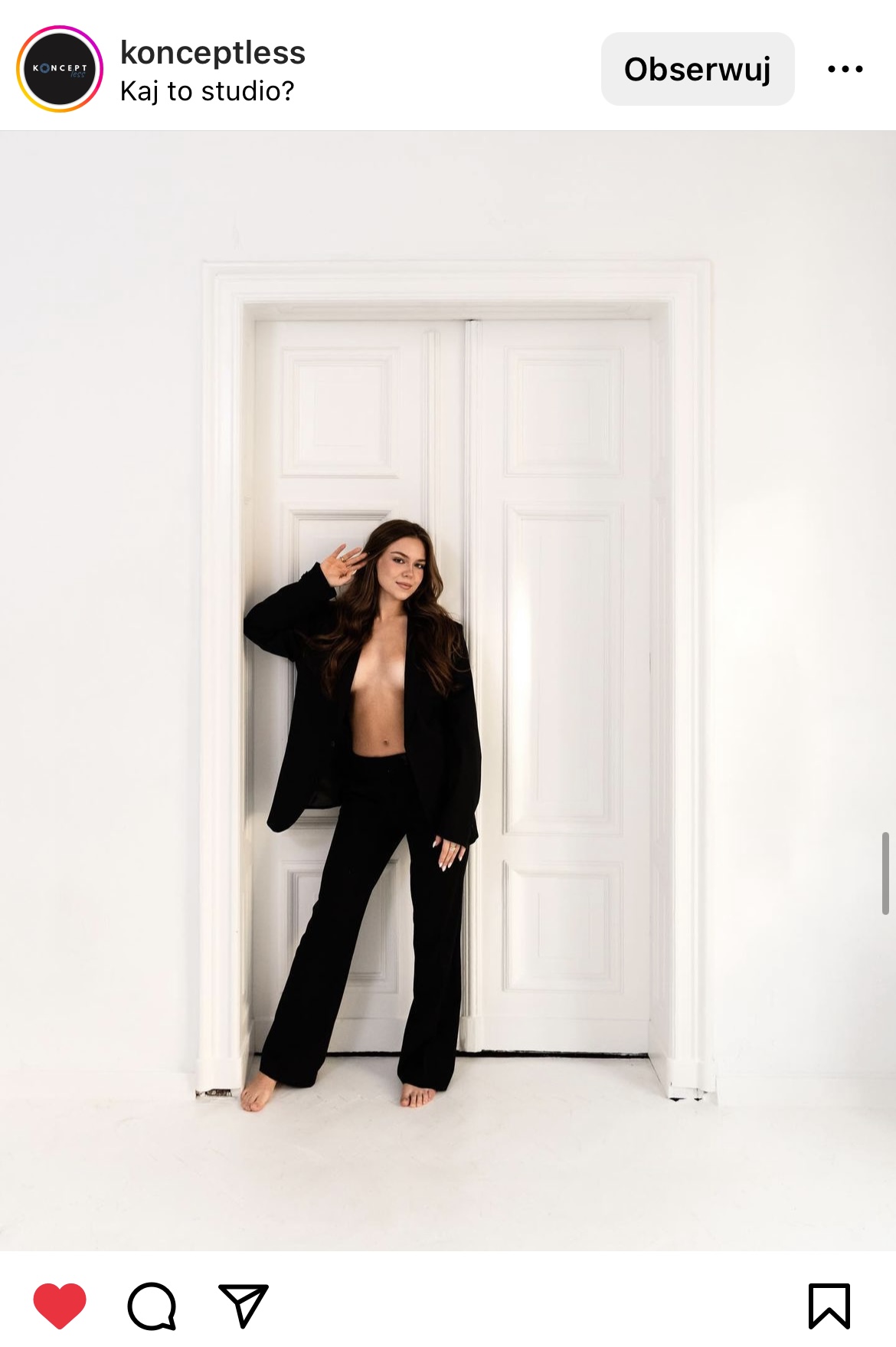 Kobieta ubrana tylko w czarny garnitur stojąca w białych drzwiach
