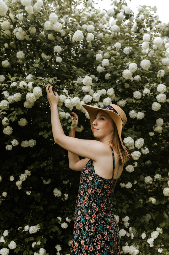 Dziewczyna w kapeluszu i sukience w kwiaty na tle drzew kwitnących na biało