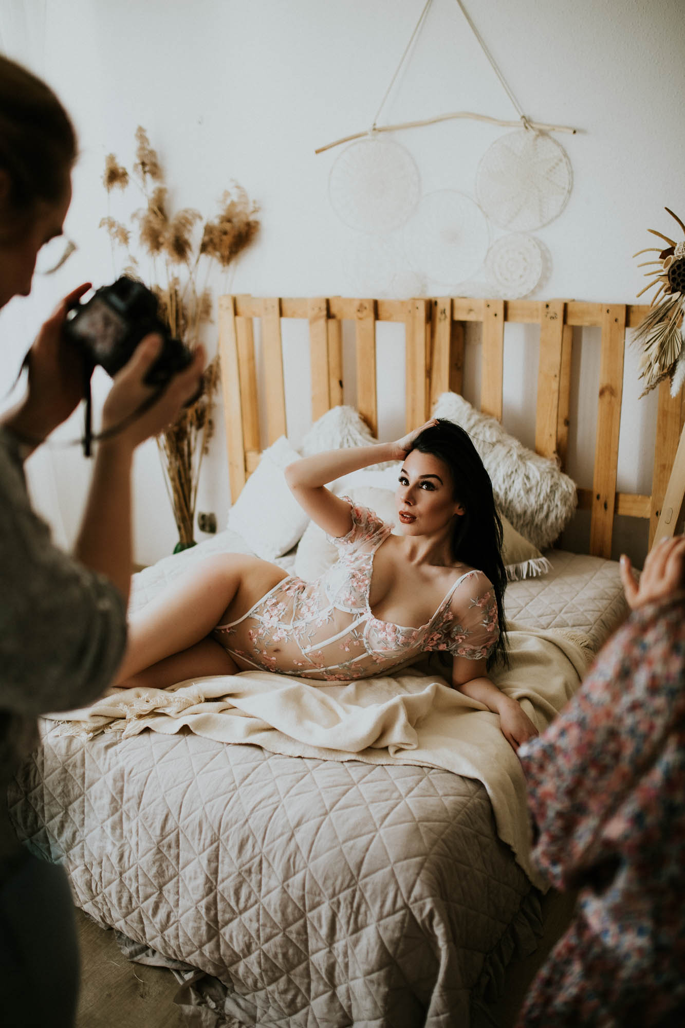 Kobieta leży na łóżku i pozuje kobiecie z aparatem