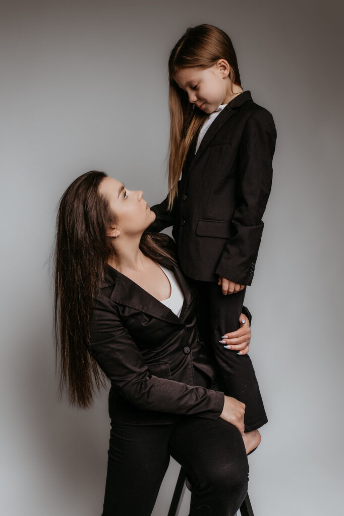 matka trzyma w ramionach córkę, ubrane są w eleganckie czarne garnitury