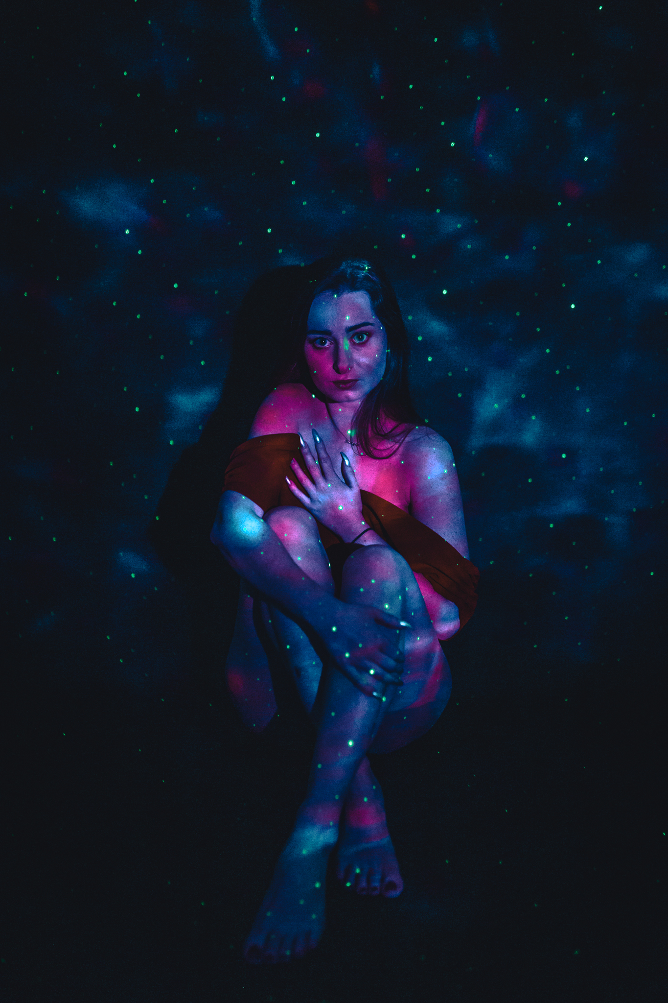 Kobieta siedzi na podłodze i zakrywa się rękoma. Ma wyraz twarzy boję się