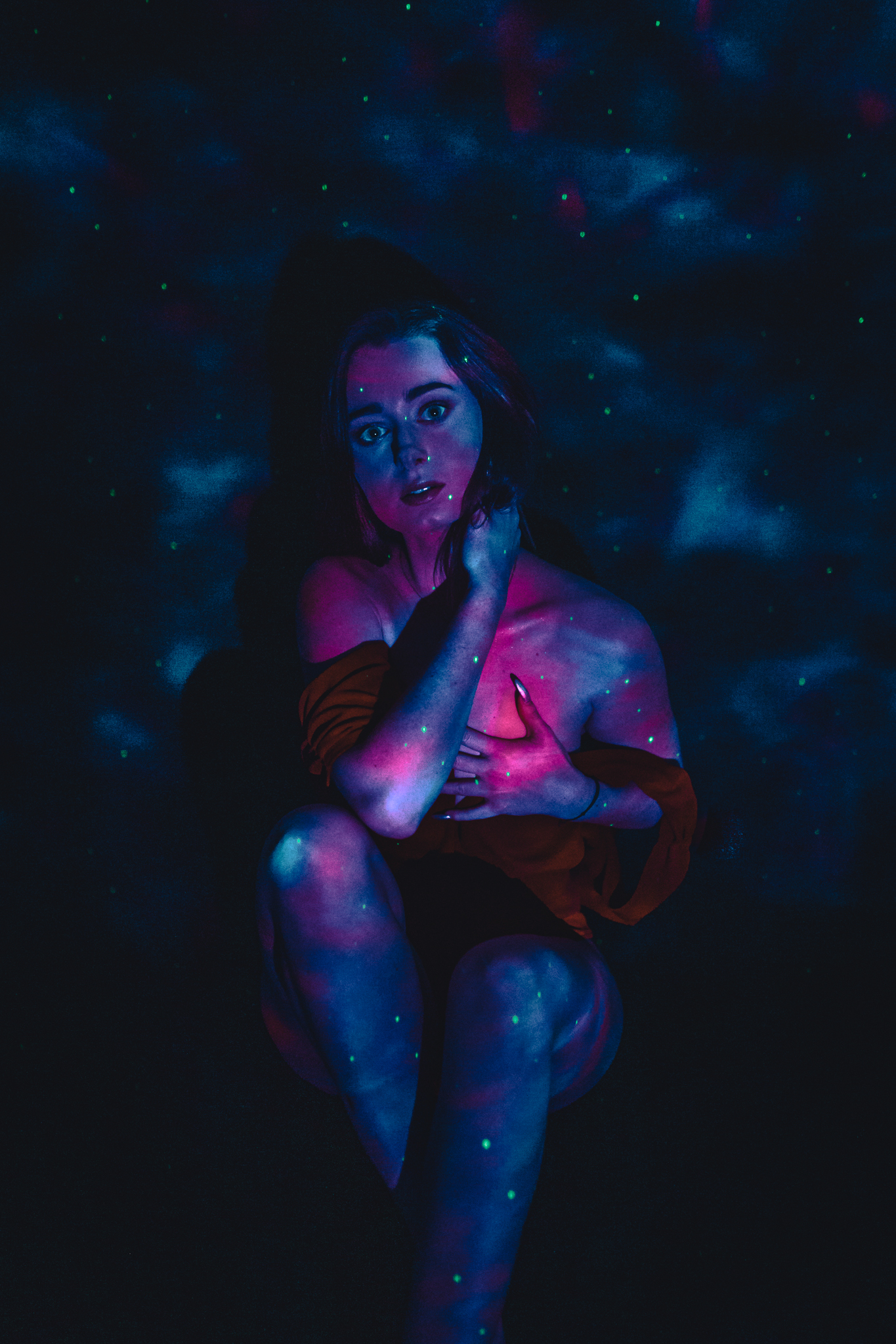 Kobieta trzyma się jedną ręką za szyję, drugą za dekold. Opada na nią sztuczne światło. Sesja zmysłowa