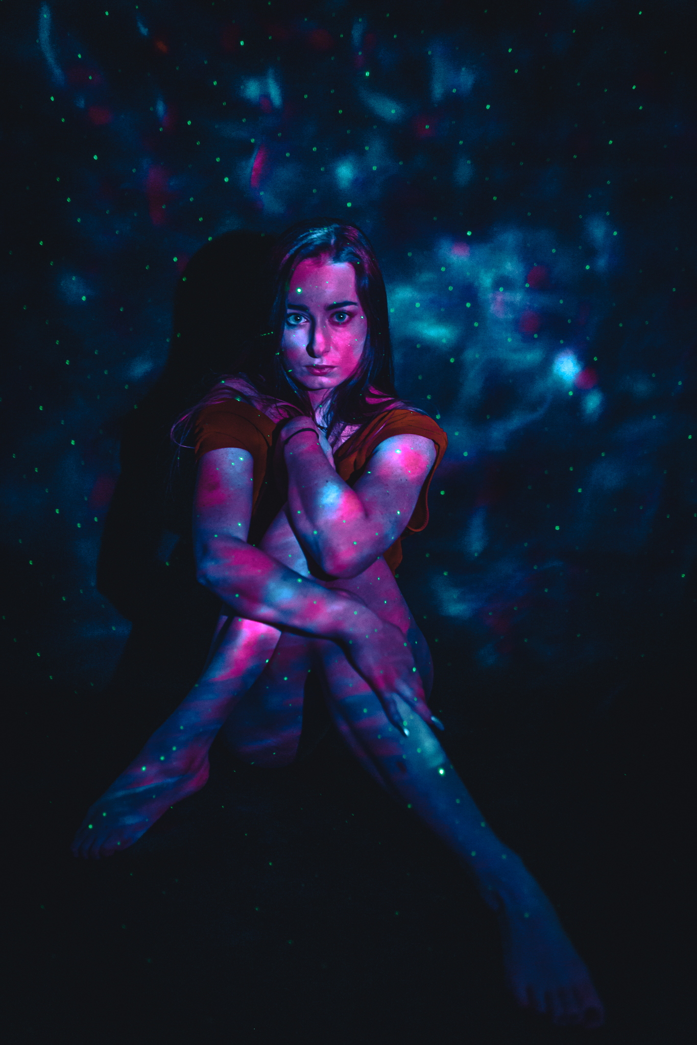 Dziewczyna siedzi na wprost obiektywu ze skrzyżowanymi nogami, ręką trzyma lewe ramie