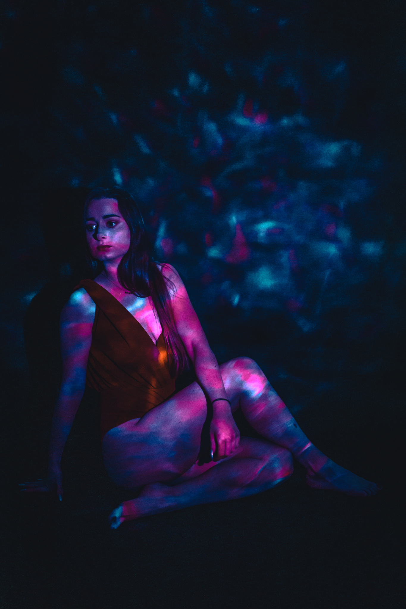 Dziewczyna w body siedzi na podłodze na jej ciało opadają promienie sztucznego światła