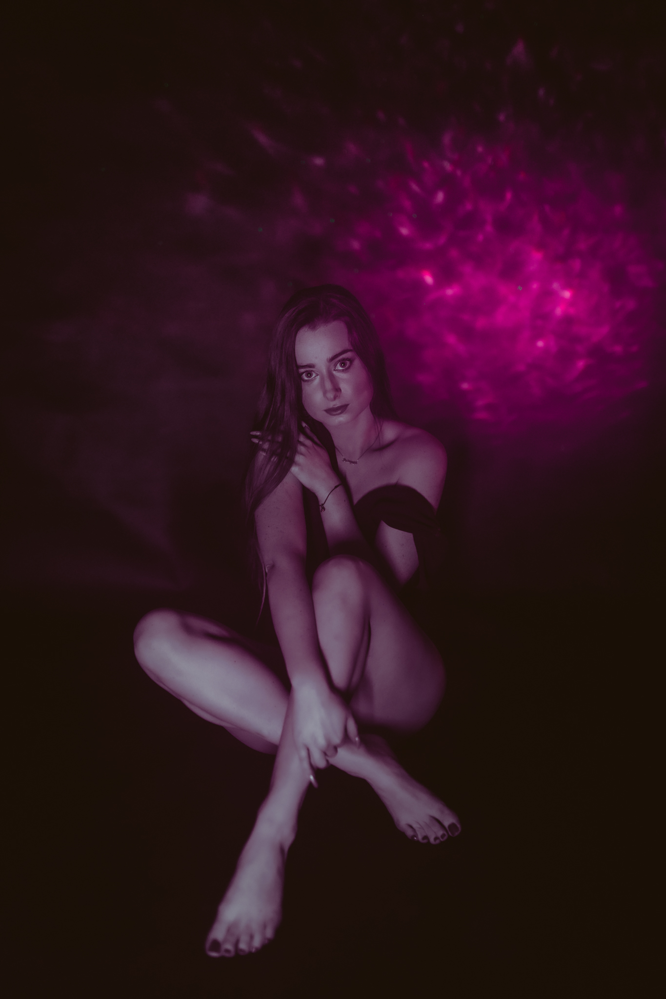 Kobieta siedząca skrzyżnie na podłodze. Patrzy w stronę obiektywu ręką dotyka włosów