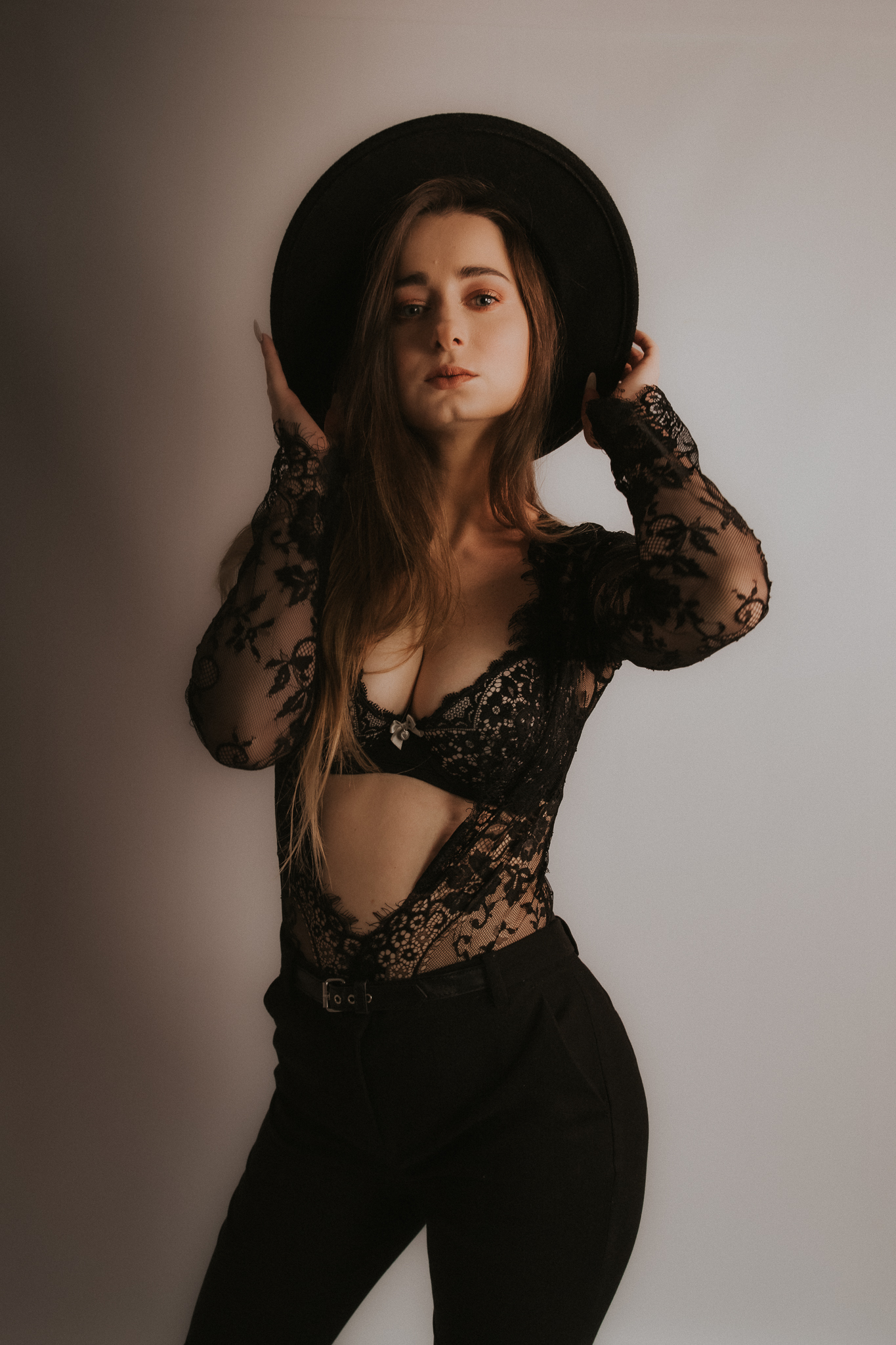 Młoda kobieta trzymająca się za kapelusz. Eksponuje swoje piękne, kobiece kształty przed obiektywem