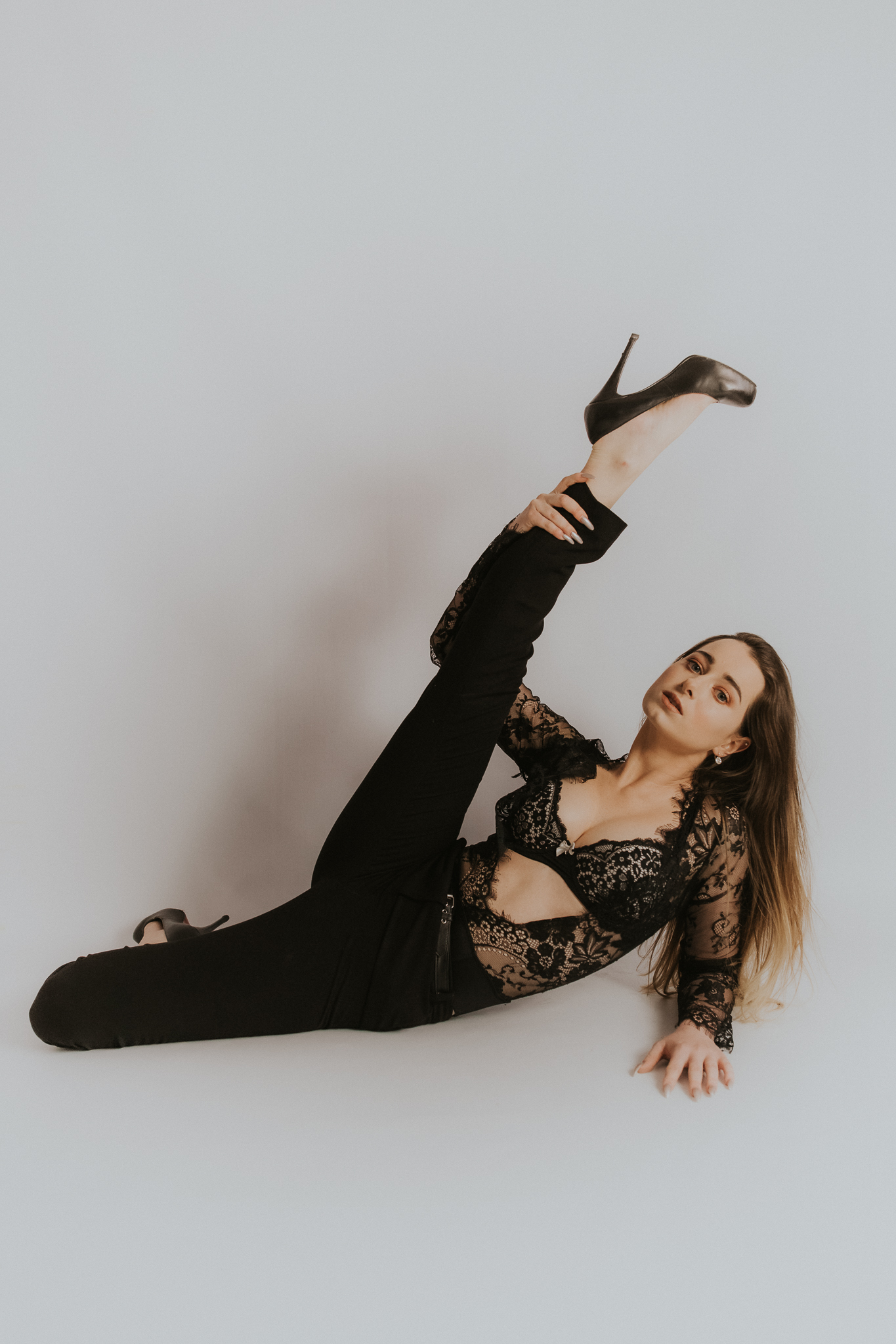 Dziewczyna pozuje na podłodze. ma nogę w górze. Eksponuje piękną, czarną szpilkę