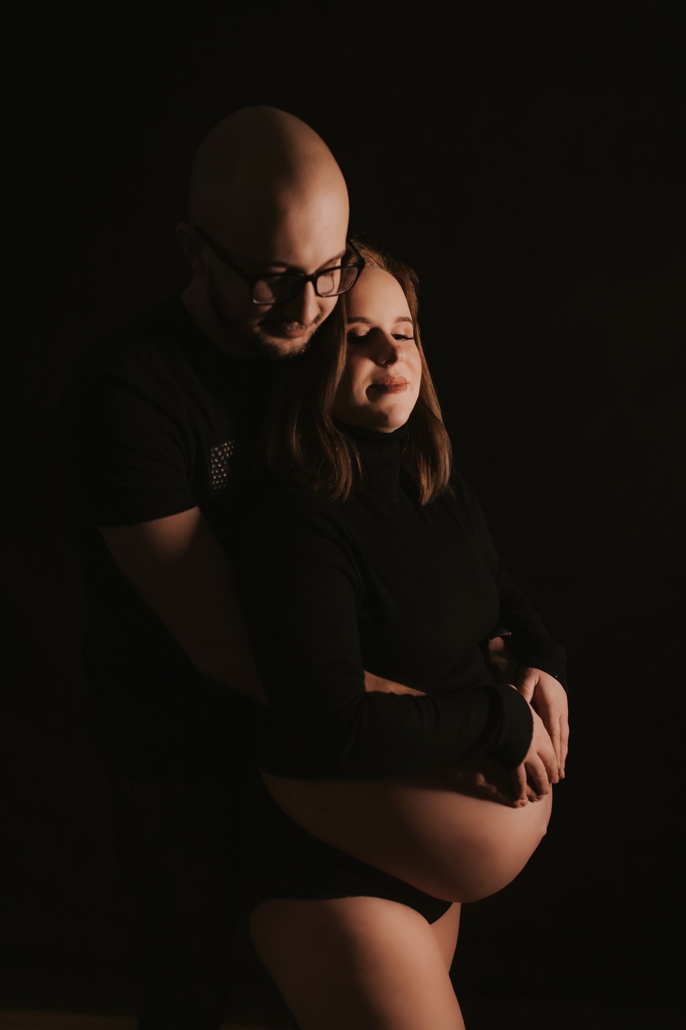 Kobieta i mężczyzna wtuleni w siebie, trzymają ręce na ciążowym brzuchu