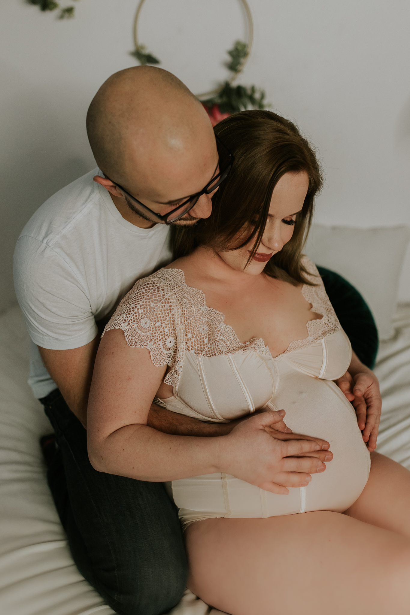 Przyszli rodzice wtuleni w siebie na łóżku. Ręce trzymają na ciążowym brzuszku