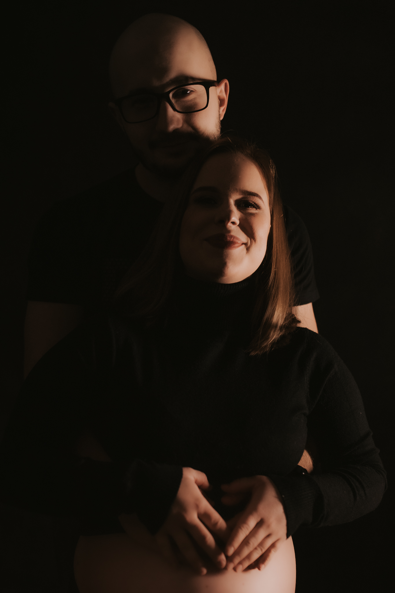 Uśmiechnięta para trzymająca się za ciążowy brzuch