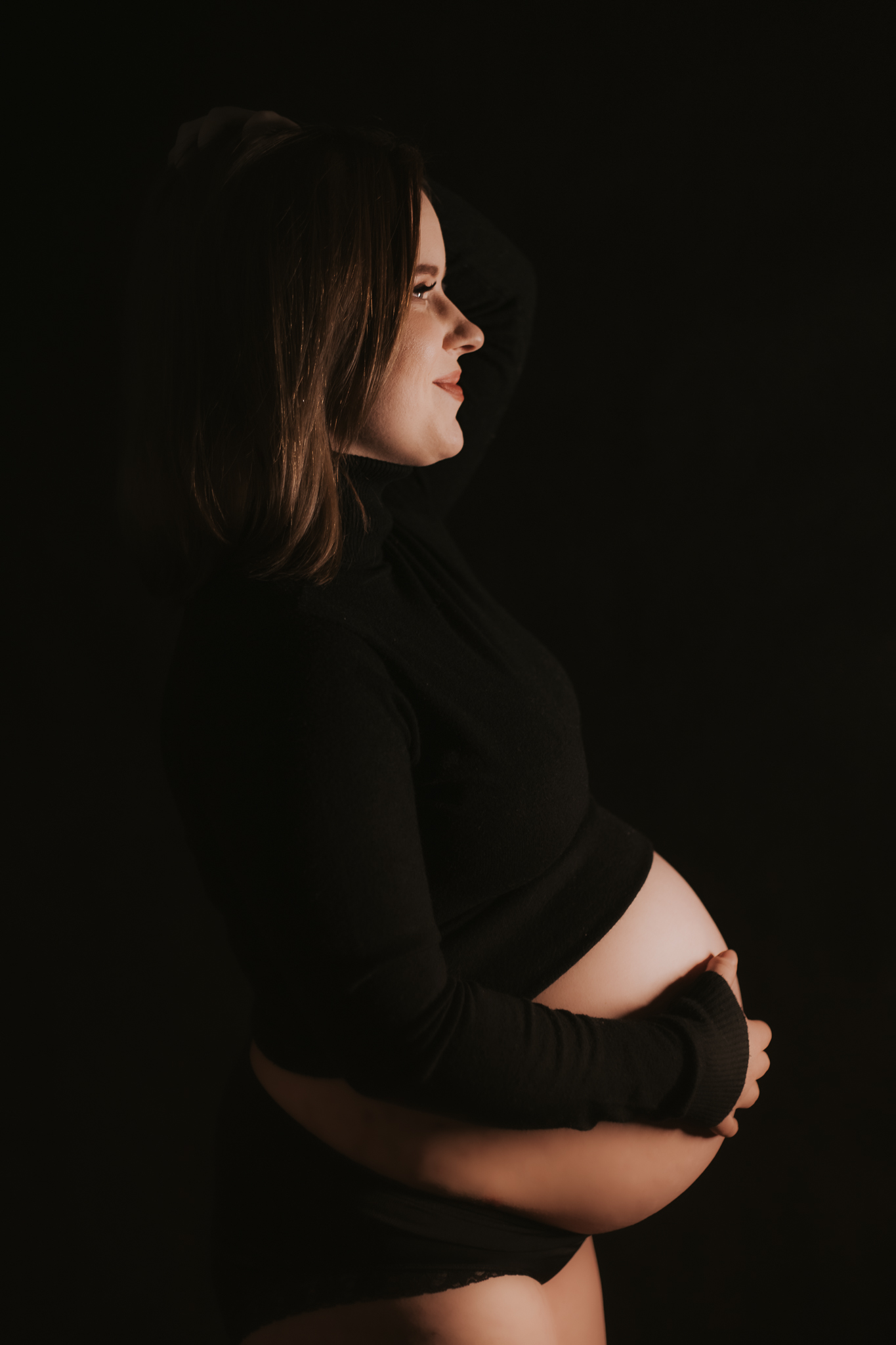 Sesja ciążowa. Kobieta trzyma się za ciążowy brzuch