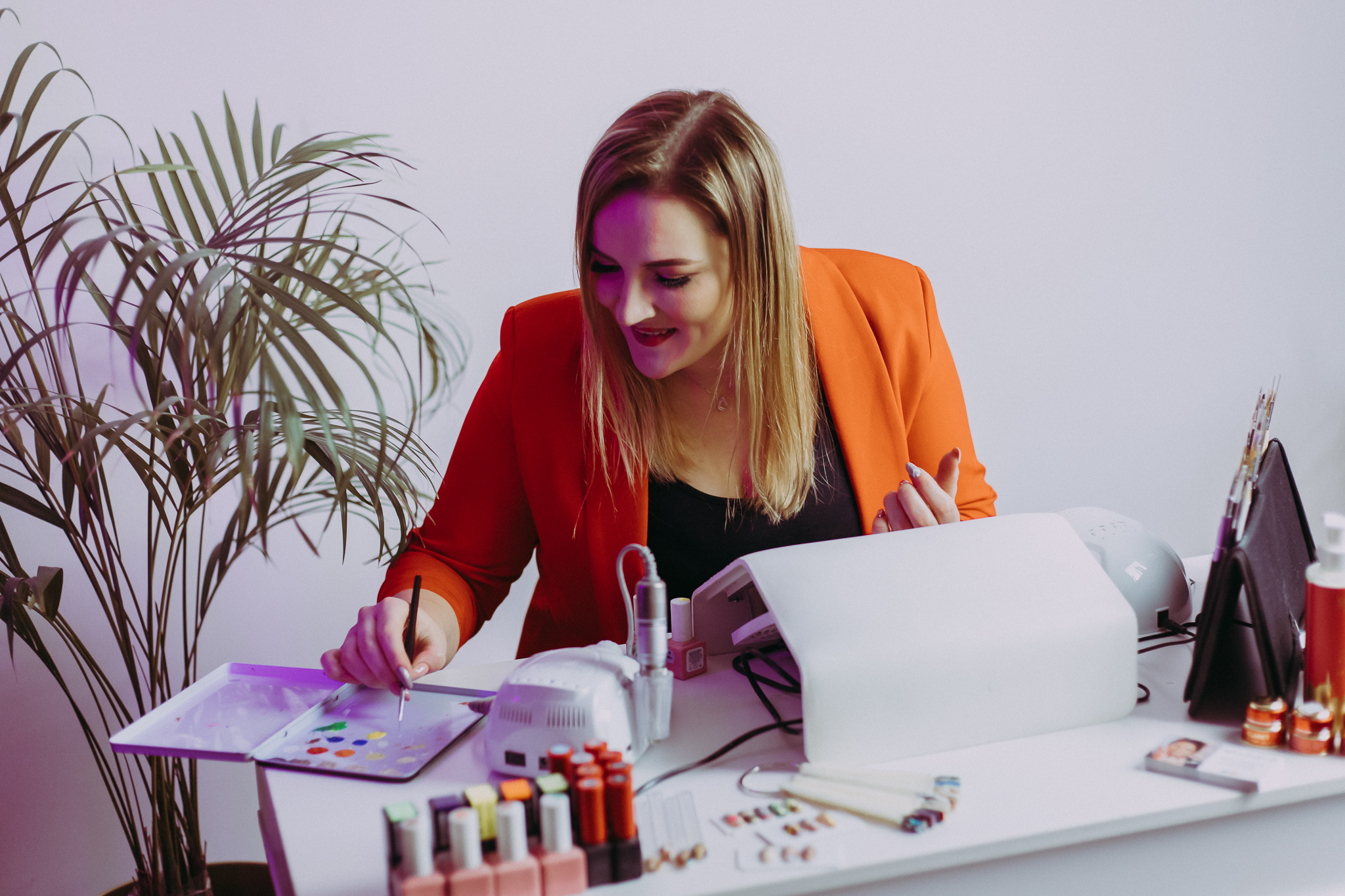 Kobieta szuka miejsca w terminarzu. Siedzi przy biurku, gdzie ma lakiery do paznokci i lampę. Sesja wizerunkowa