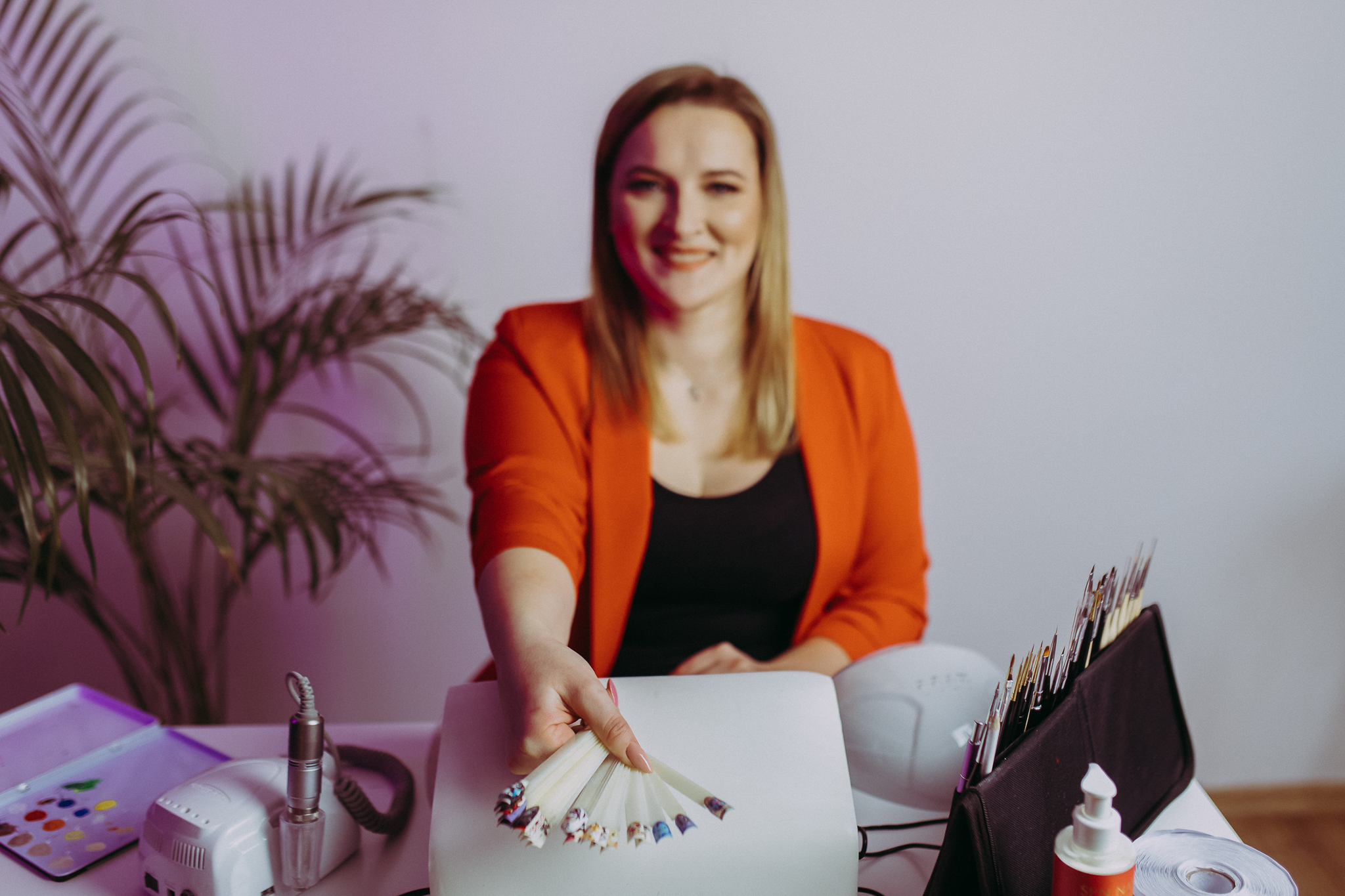 Kobieta pokazuje paletę kolorów lakierów do paznokci opartych o lampę