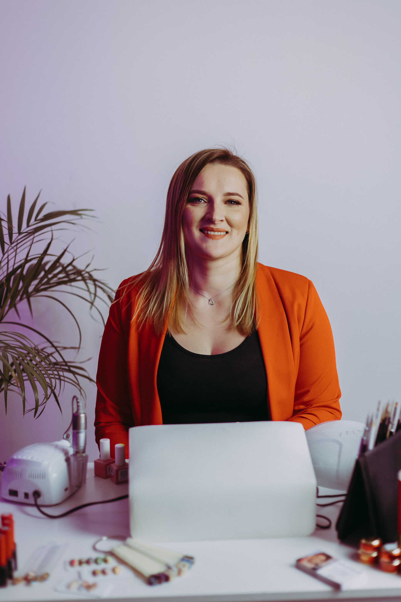 Uśmiechnięta blondynka zza stołu z lampą do paznokci i akcesoriami