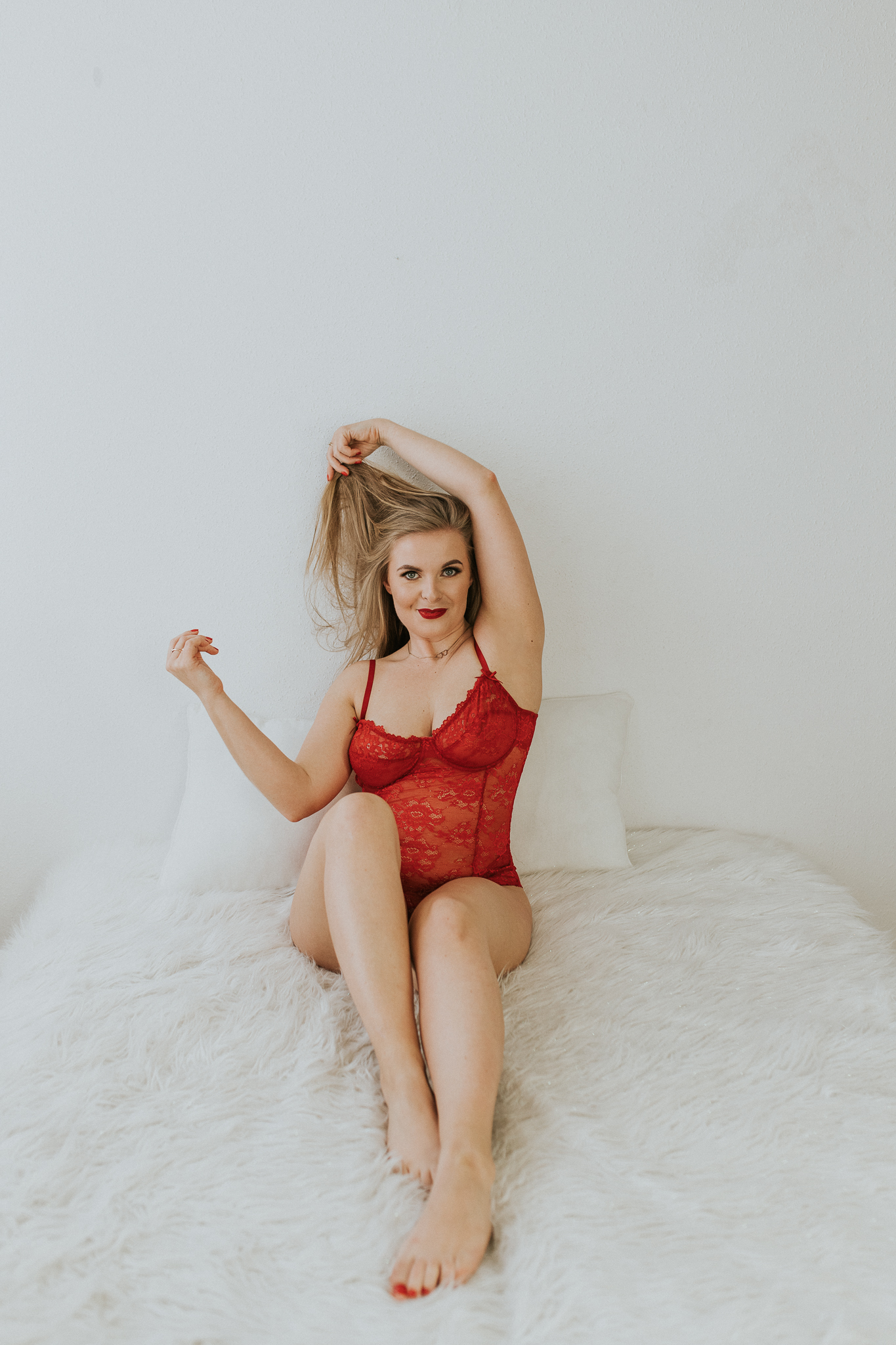 Kobieta, która siedzi na łóżku w czerwonym body i bawi się włosami.