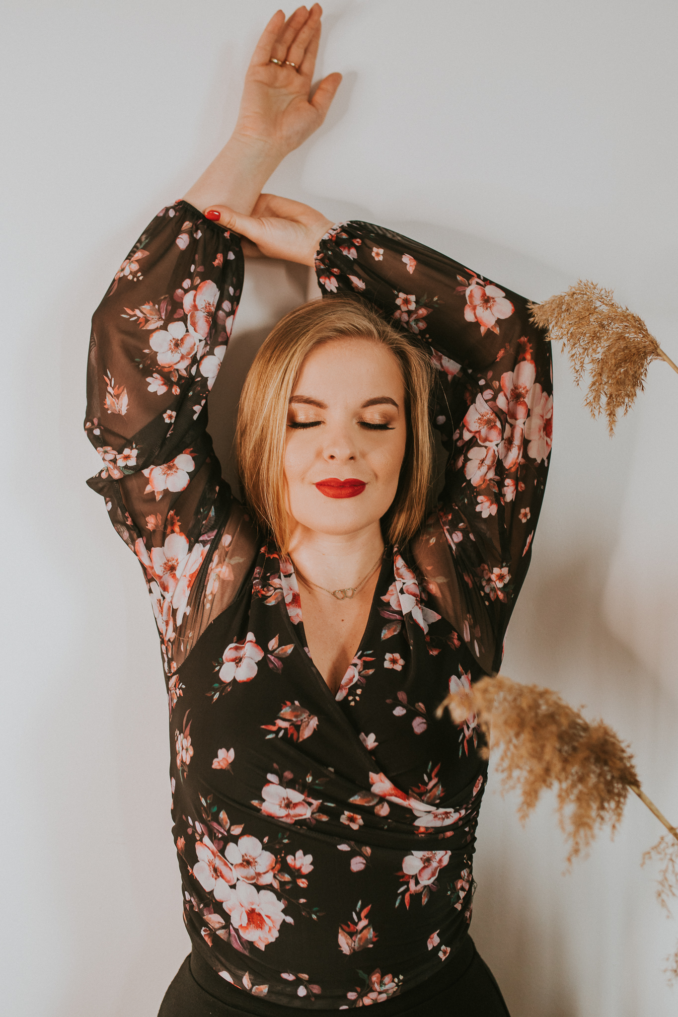 Piękna kobieta w kwiecistej bluzce oparta o ścianę