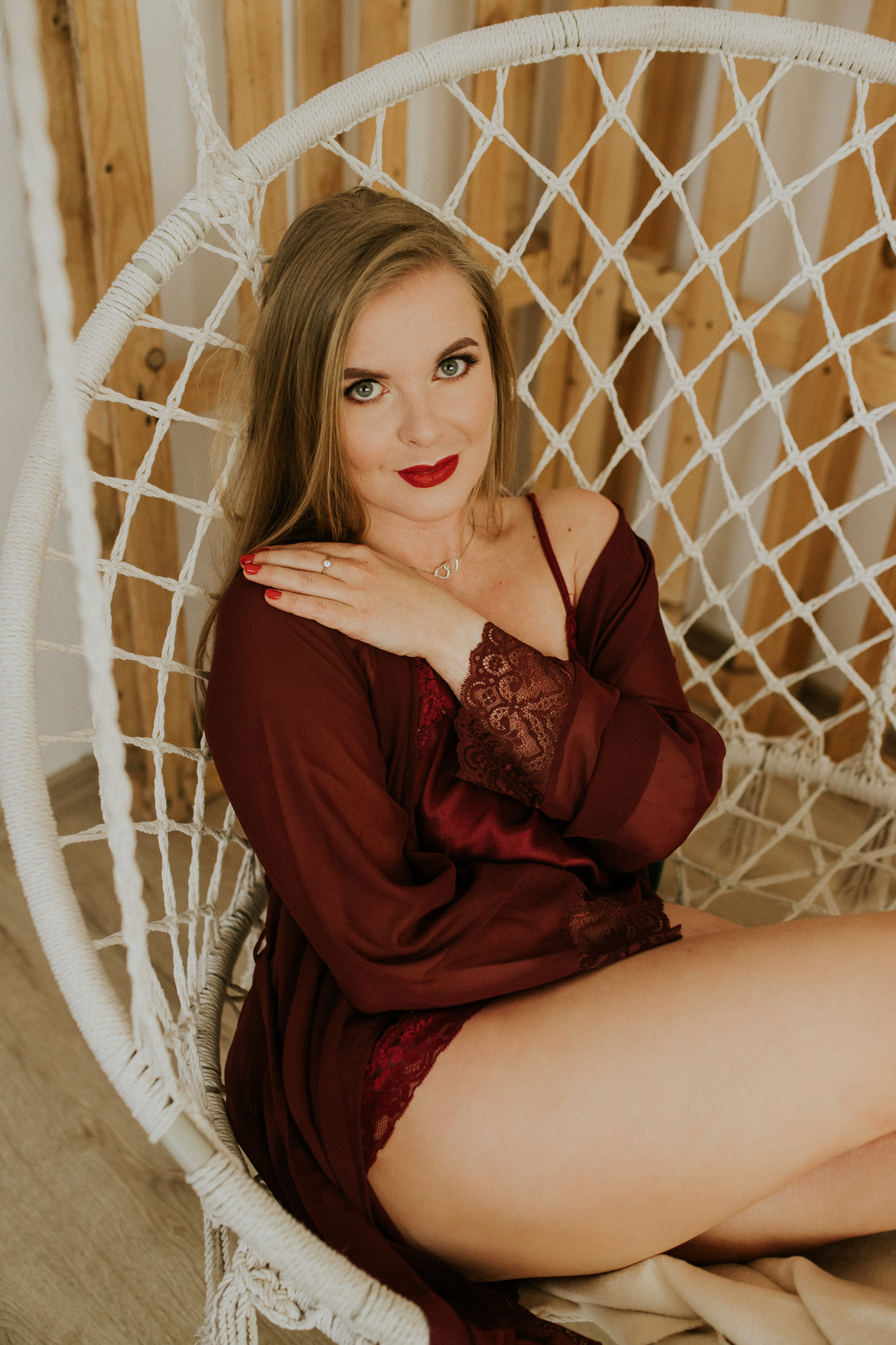 Blondynka ubrana w czerwień, siedzi na białej huśtawce i uśmiecha się