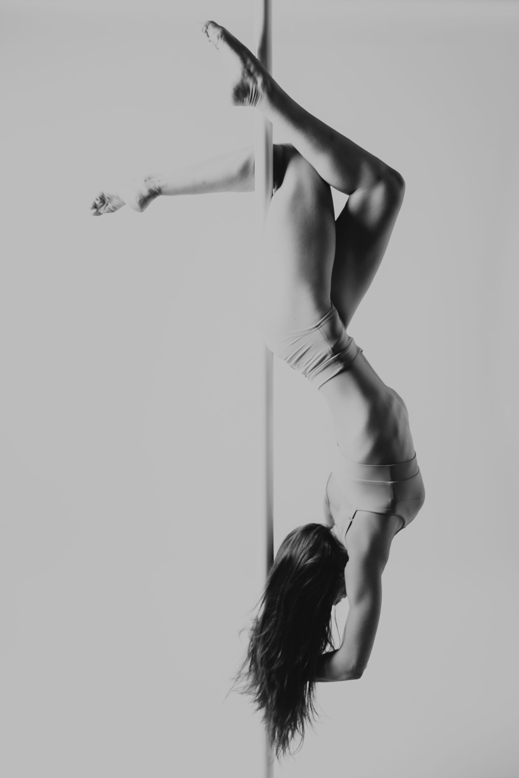 Kobieta dotykająca głową rury do góry nogami. Ma splecione nogi