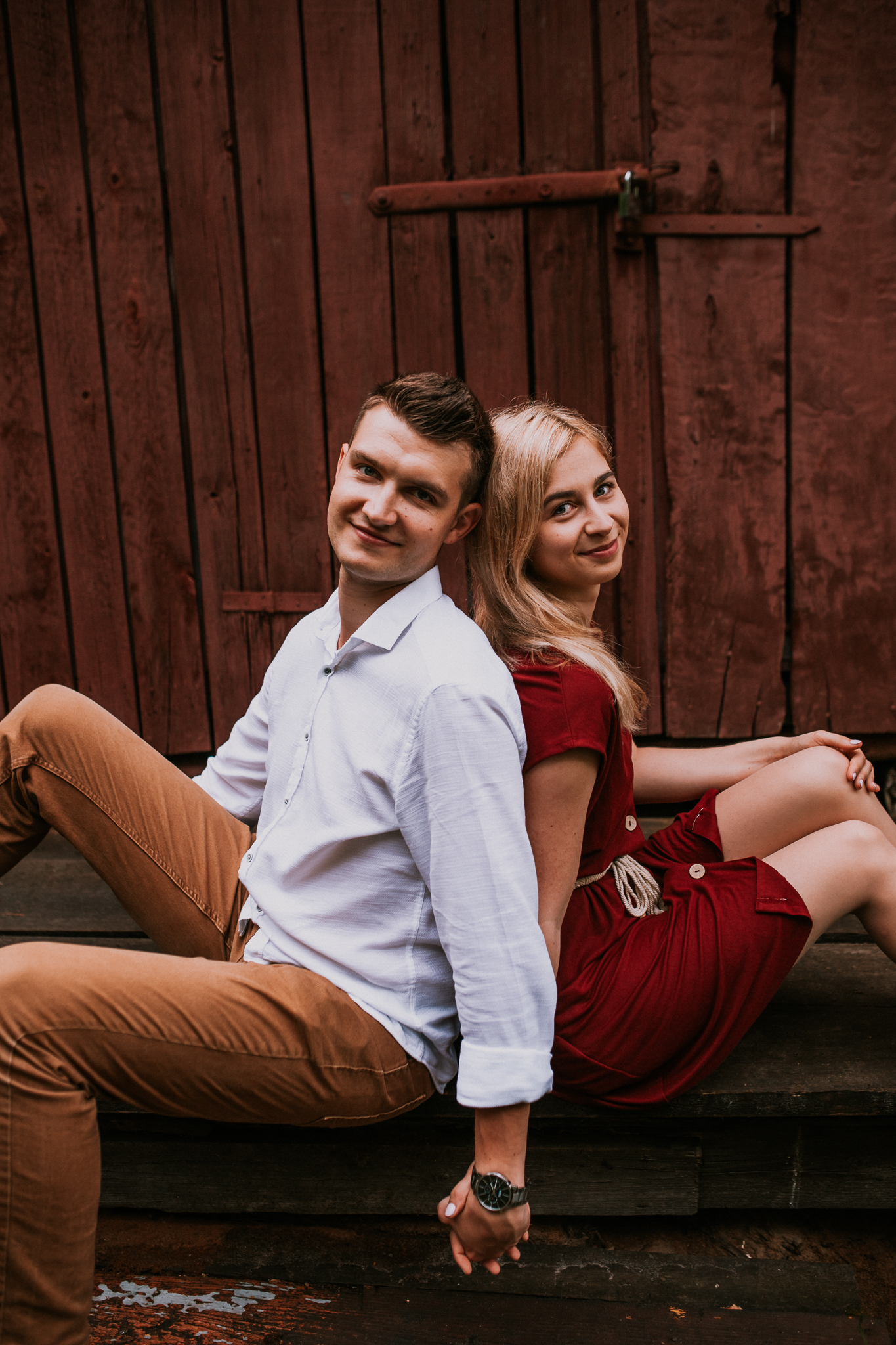 Mężczyzna i kobieta siedzą do siebie plecami. Patrzą się w stronę obiektywu, są uśmiechnięci