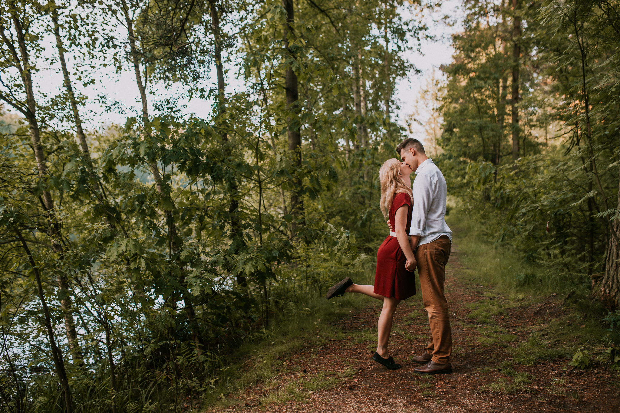 Dziewczyna całuje chłopaka podczas spaceru. Ma uniesione kolano. Sesja narzeczeńska