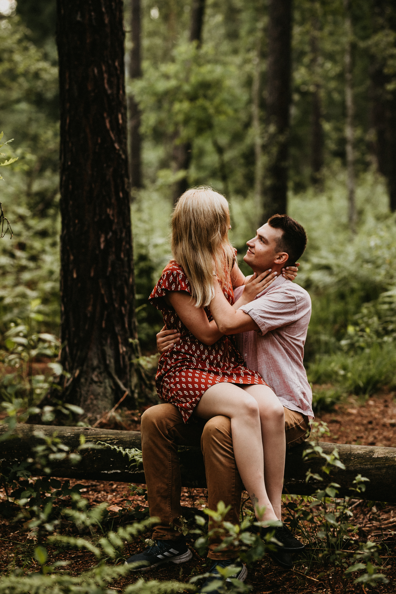 Para siedzi na drzewie, które leży na ziemii. Przytulają się. Sesja narzeczeńska w plenerze