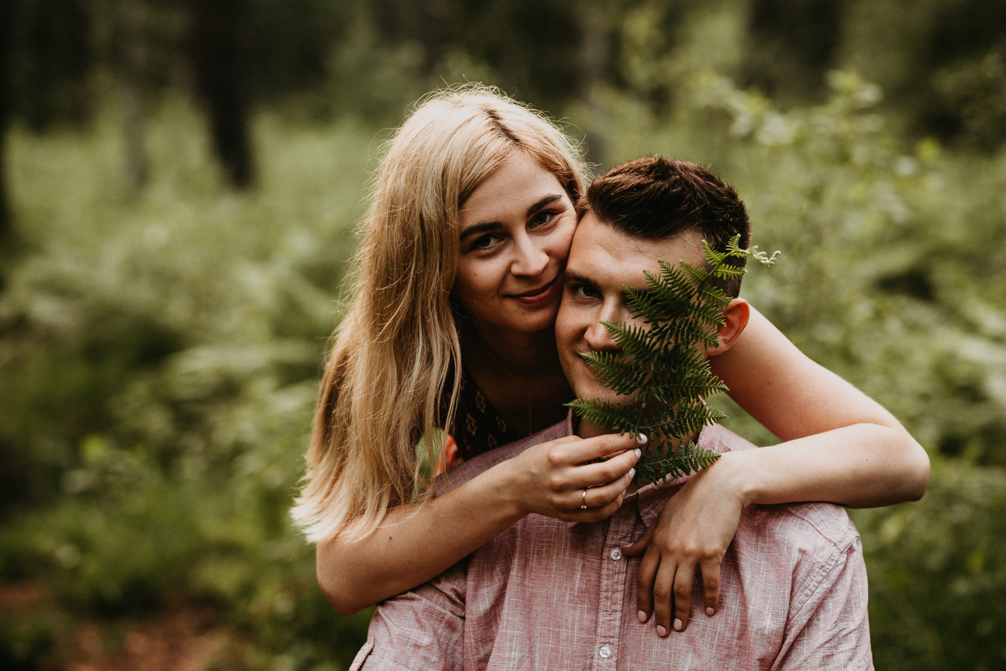 Dziewczyna nachylona nad mężczyzną. W ręce trzyma liść paproci, który zasłania mu trochę twarzy