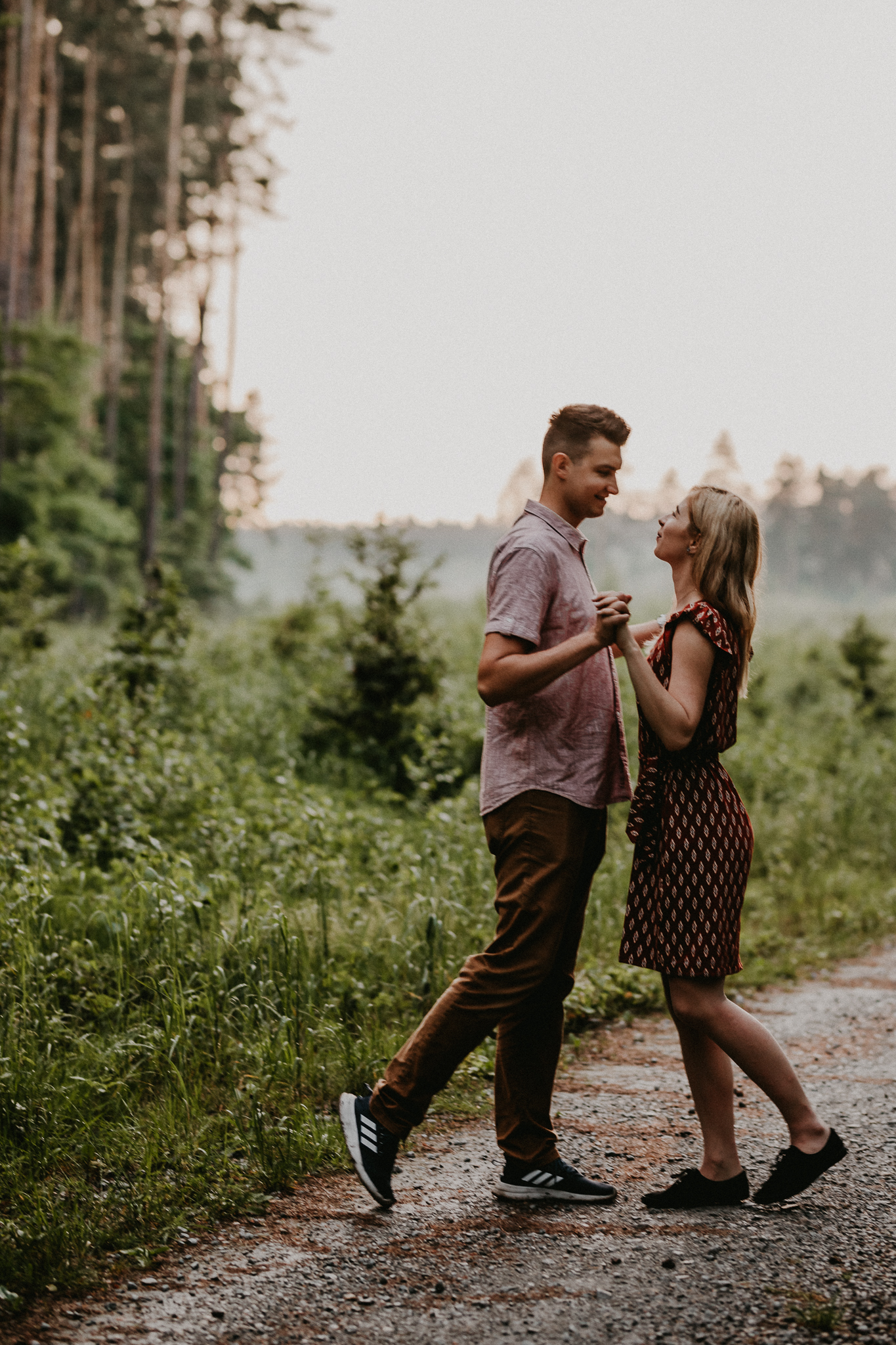 Para trzyma się za ręce i uśmiecha się do siebie pośród spaceru leśną ścieżką