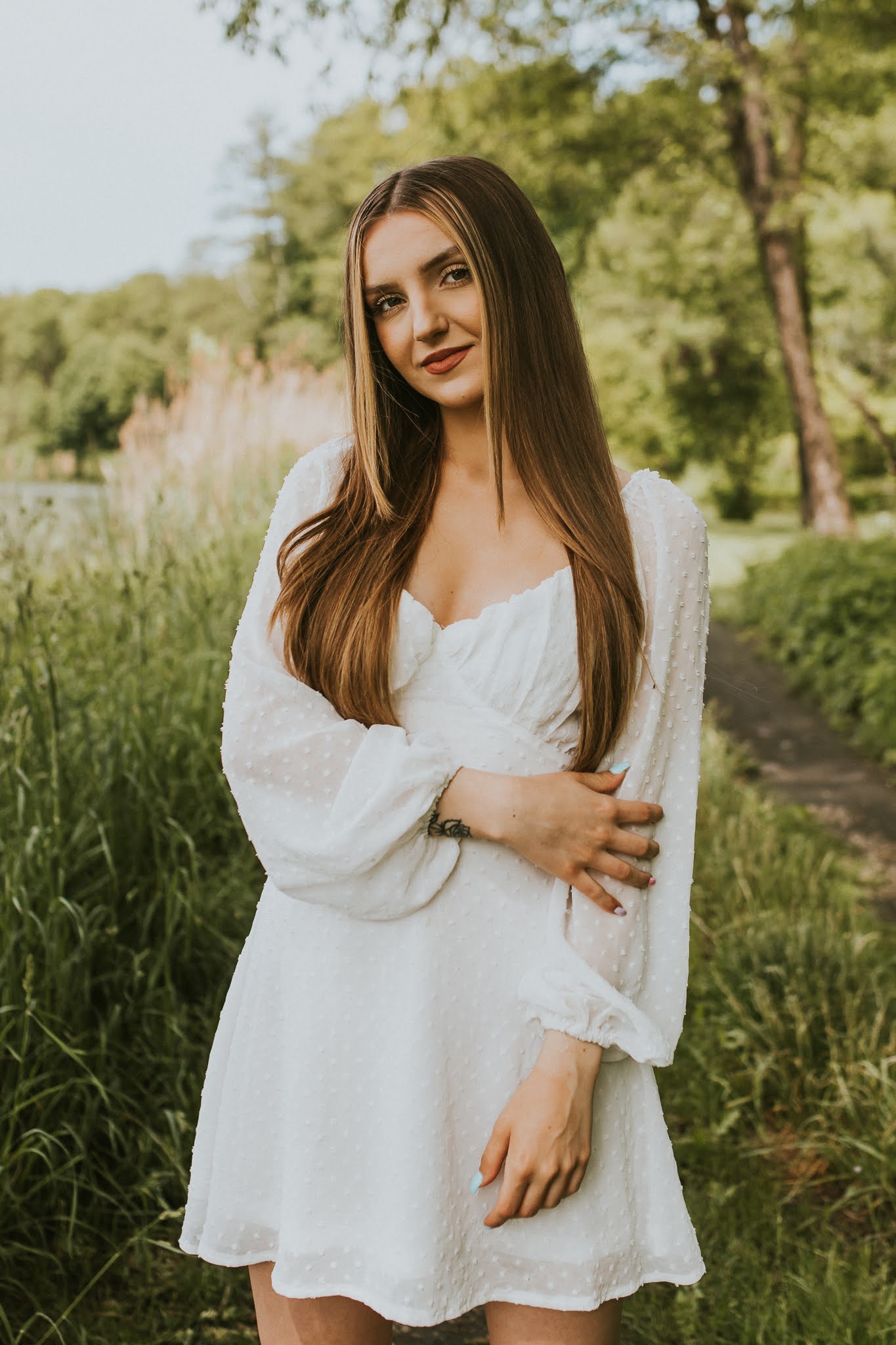 Piękna dziewczyna w białej sukience. Jedną ręką trzyma rękaw swojej sukienki.