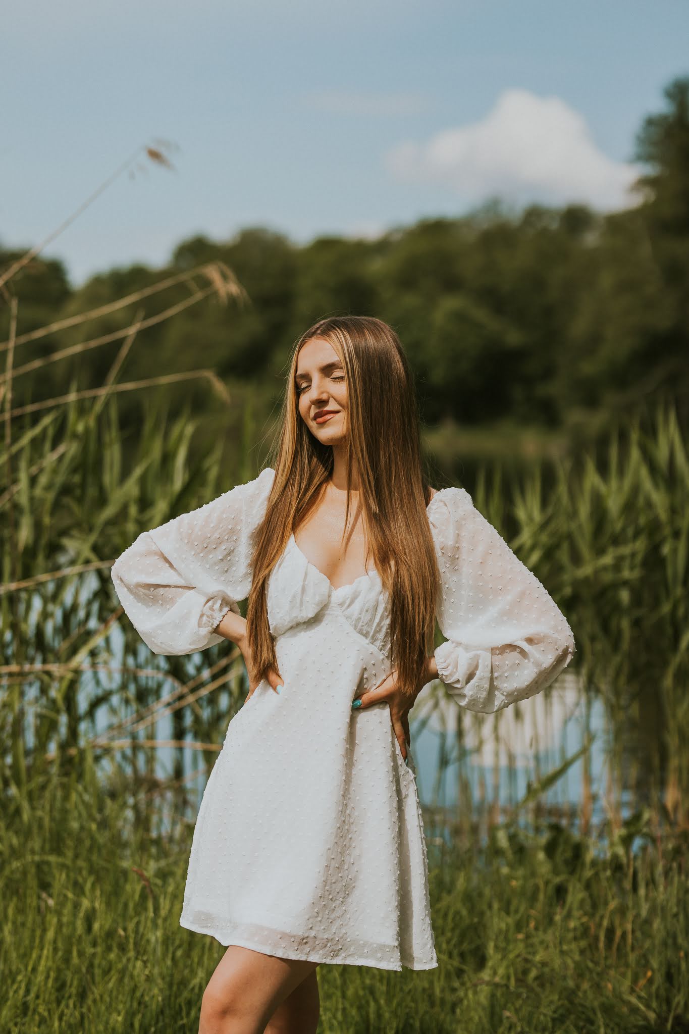 Piękna dziewczyna trzyma się za boki swojej talii. W tle jezioro.