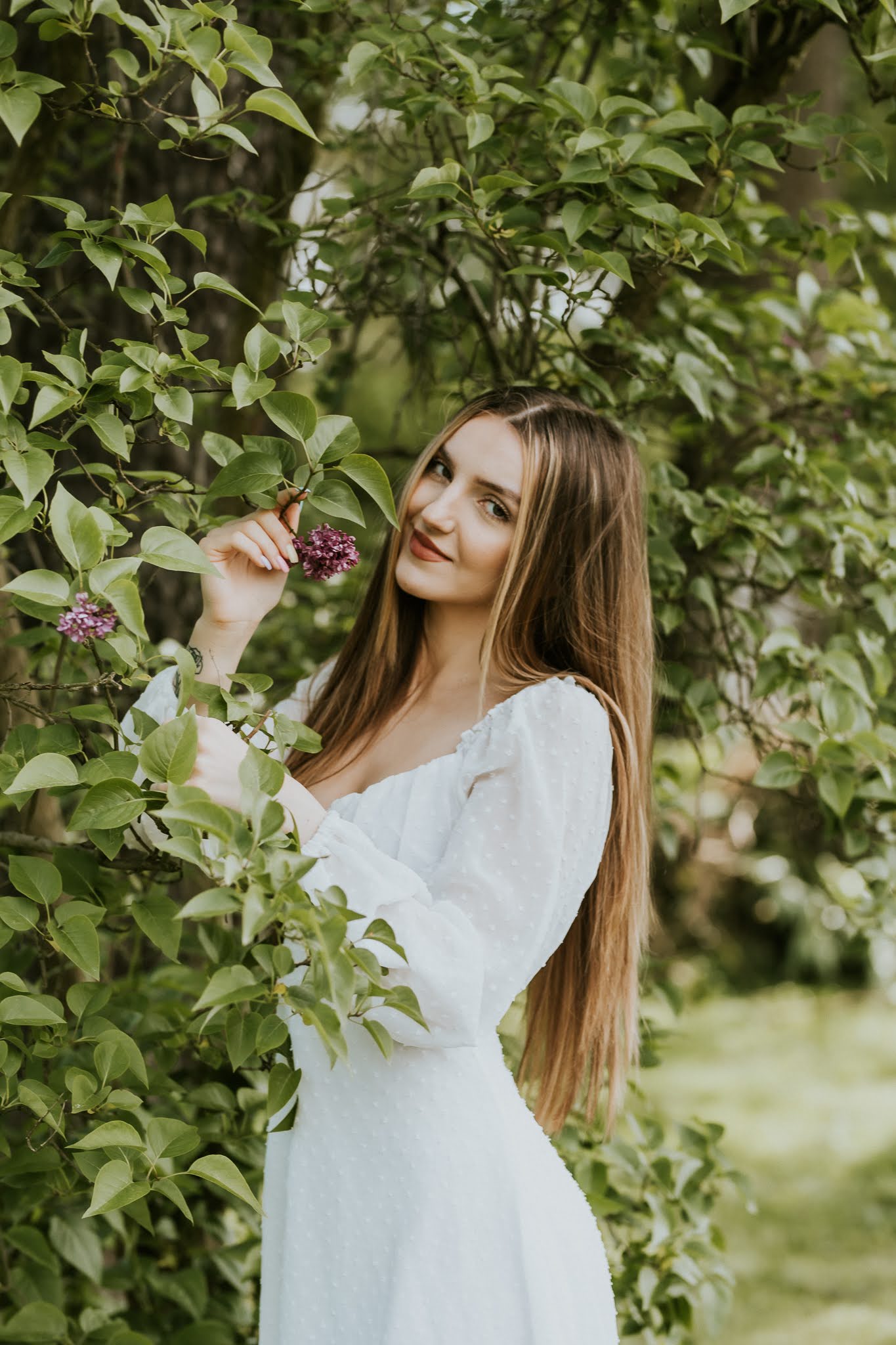 Młoda kobieta pośród liści. W ręku trzyma gałązkę.