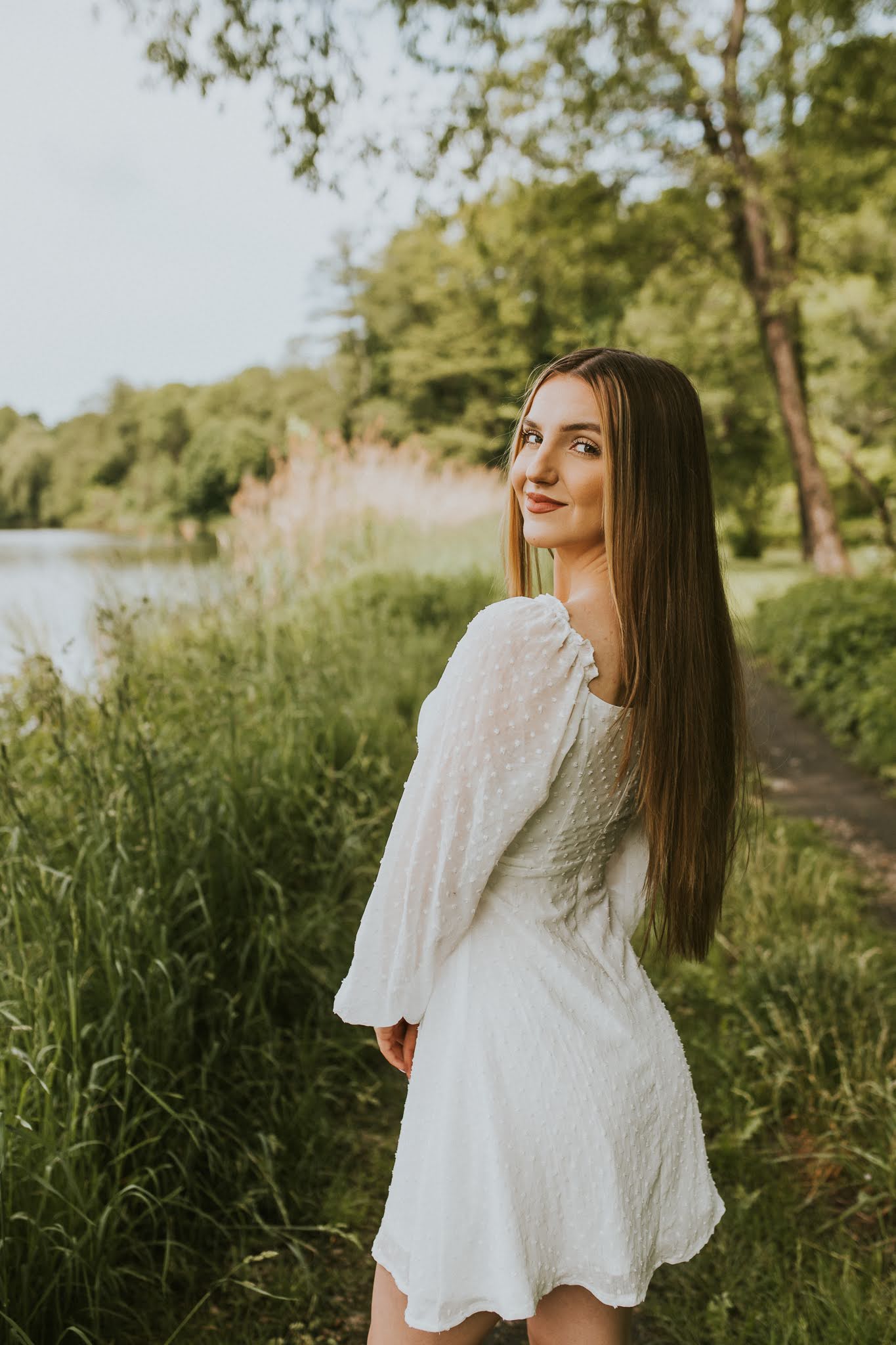 Dziewczyna odwrócona bokiem do aparatu. W tle jezioro i tatarak.