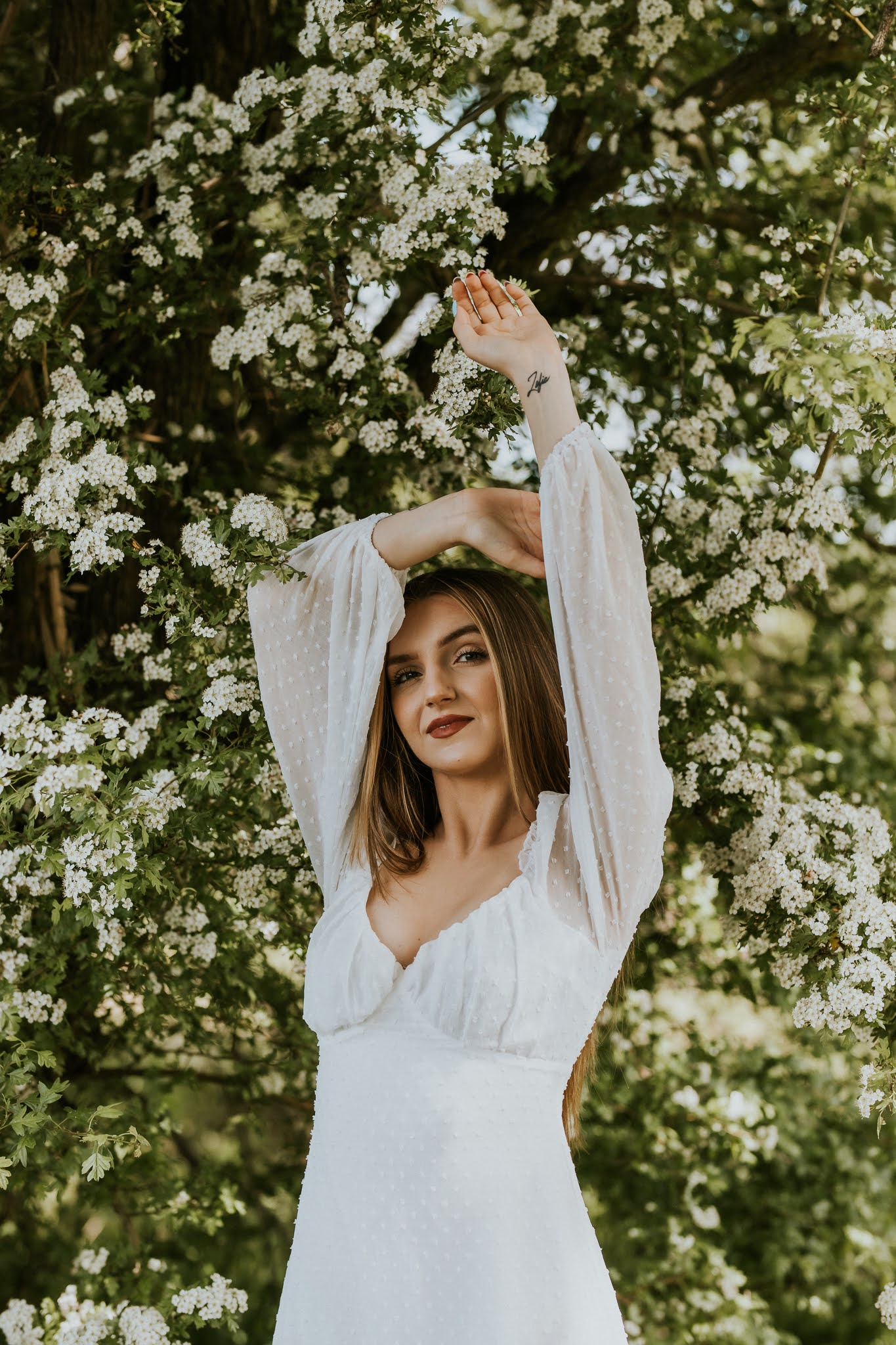 Młoda kobieta z wyciągniętymi rękoma nan tle kwitnącego drzewa