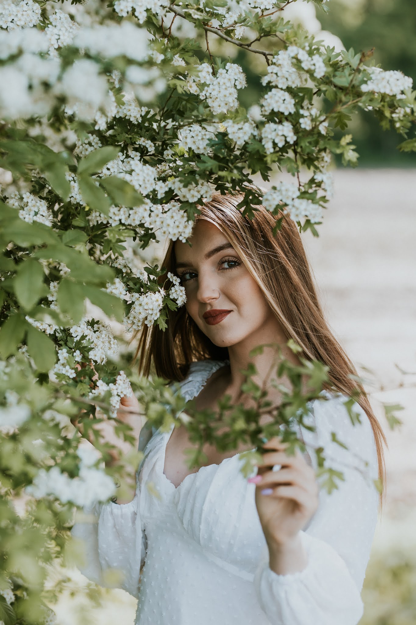 Dziewczyna w tle drzewa. W ręku trzyma kawałek gałązki