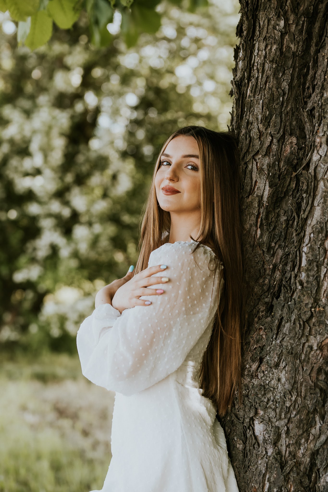 Dziewczyna ze skrzyżowanymi rękoma, oparta o drzewo