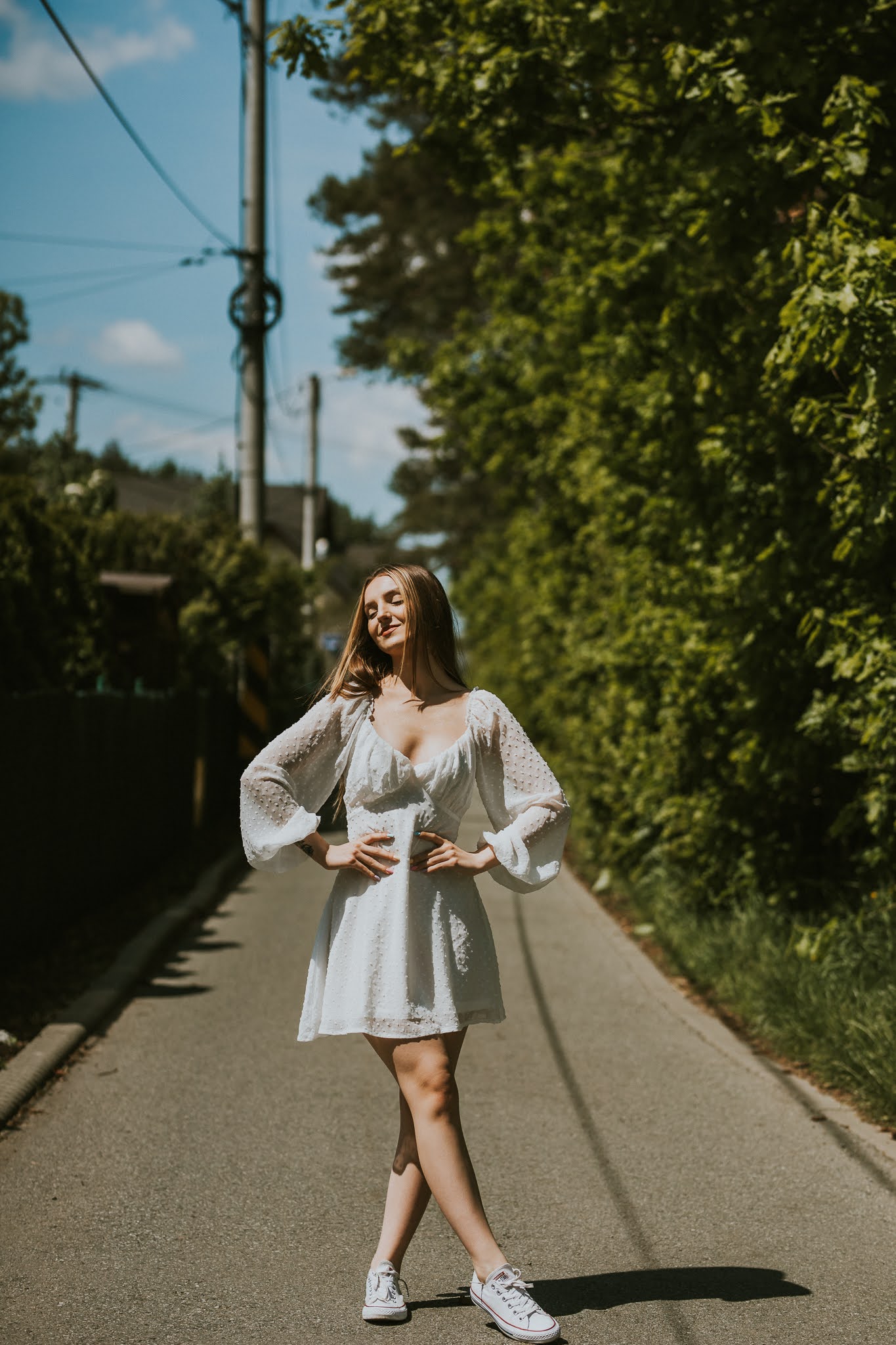 Uśmiechnięta dziewczyna z rękoma zgiętymi w talii idzie przez środek ulicy