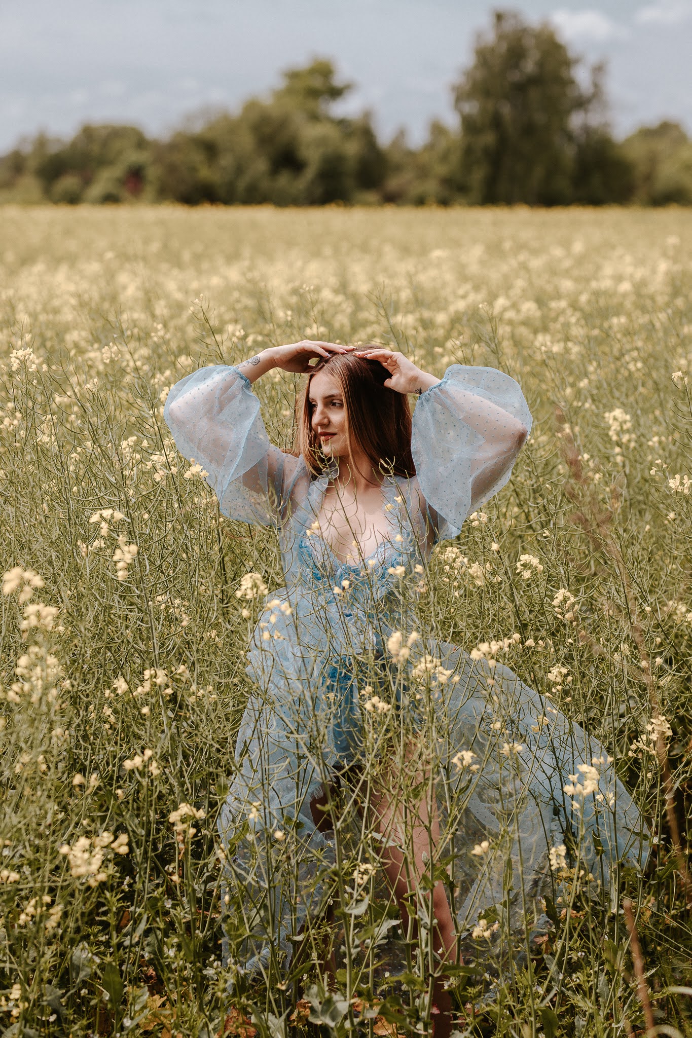 Delikatnej urody dziewczyna stoi w rzepaku i ręce trzyma na głowie