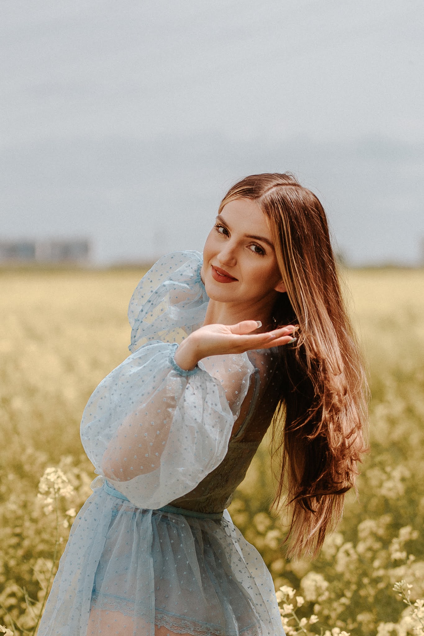 Stojąca bokiem w rzepaku dziewczyna z wyciągniętą dłonią