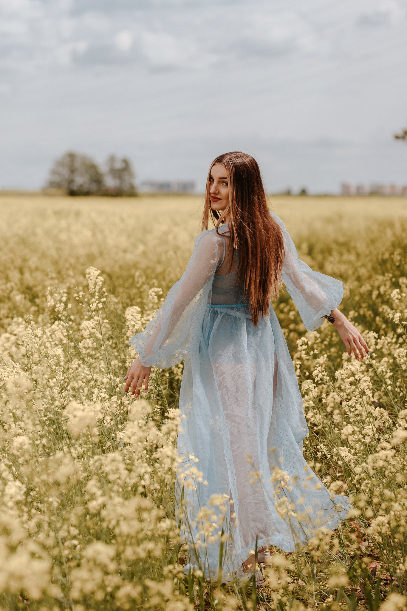 Dziewczyna spacerująca w rzepaku w błękitnej sukience