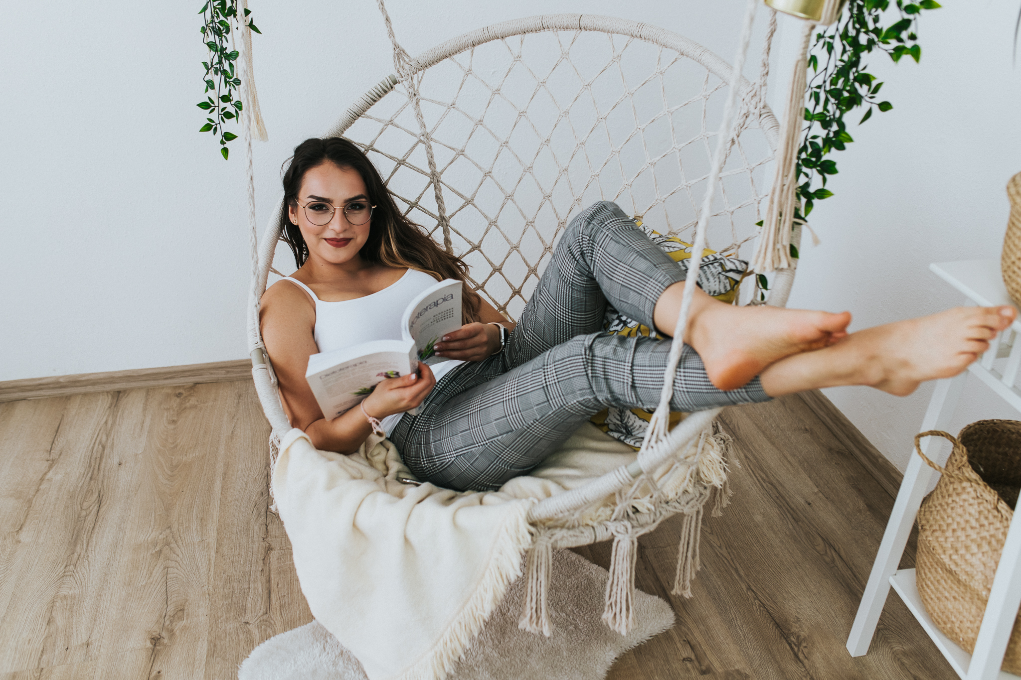 Uśmiechnięta kobieta, siedząca wygodnie i czytająca książkę na wiszącej huśtawce