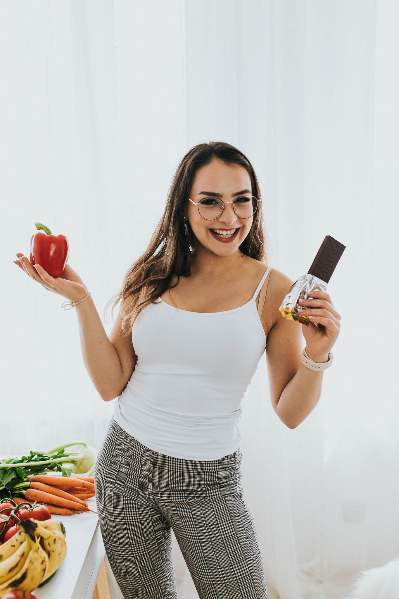 Uśmiechnięta kobieta, która w prawej ręce trzyma baton, a w lewej paprykę